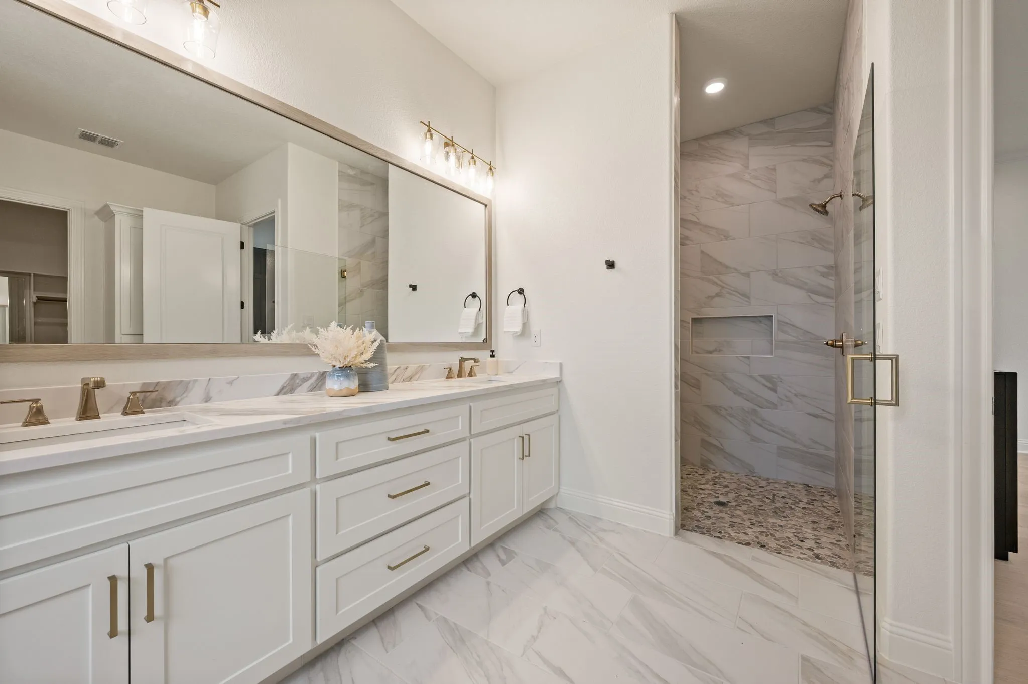 Spacious bathroom featuring a dual vanity with white cabinetry, a large frameless mirror, and brass hardware