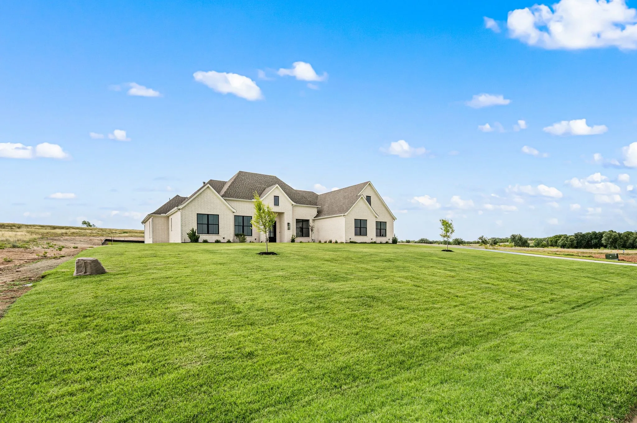 Single-story residence featuring a light-colored brick exterior, dark-framed windows, a multi-gabled roofline, and an expansive manicured lawn