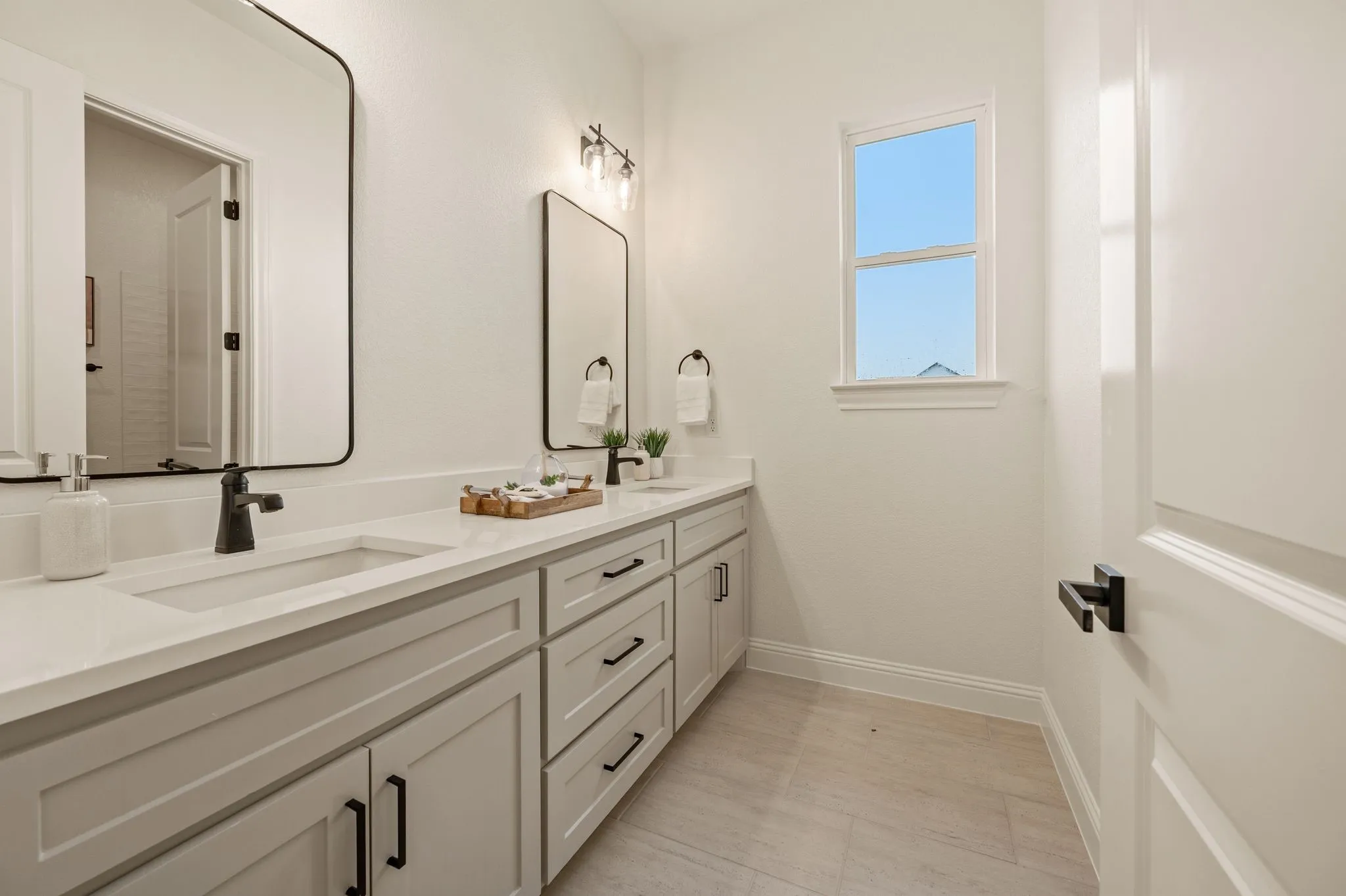 Dual vanity with light gray cabinetry, integrated sinks, black fixtures, and framed mirrors
