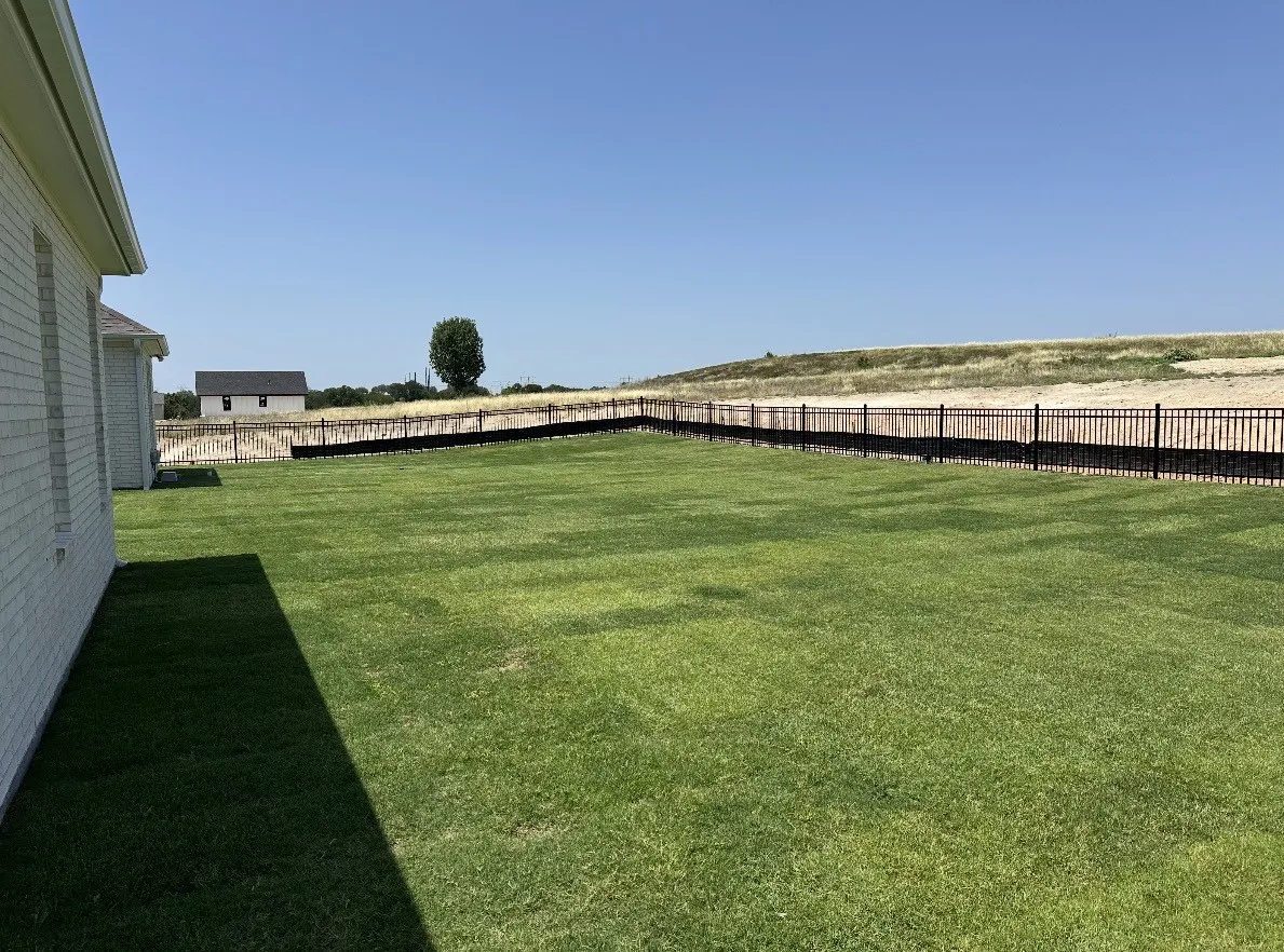 Expansive green lawn bounded by a black metal fence