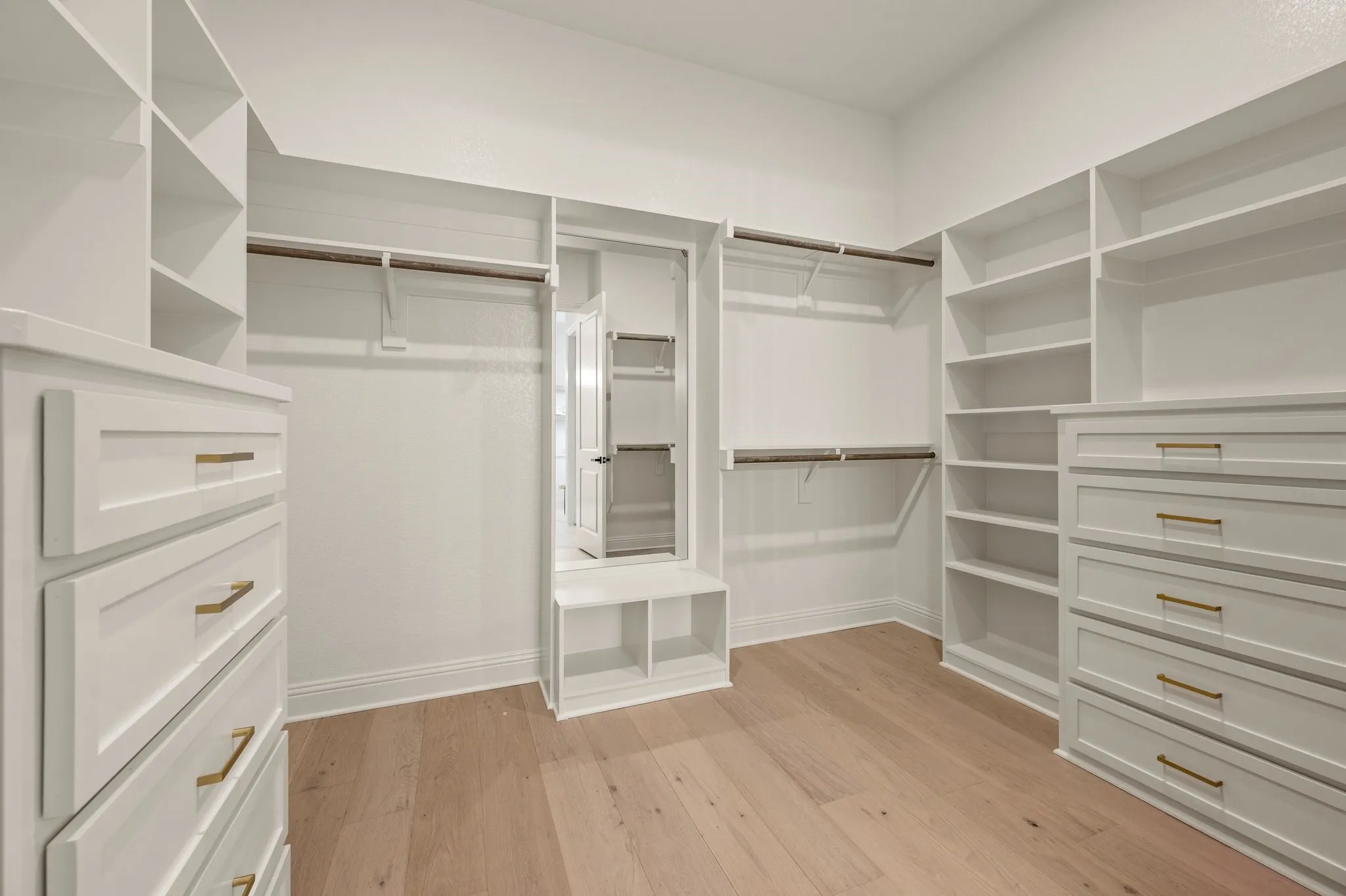 Custom closet system featuring extensive shelving, built-in drawer units with gold-tone hardware, multiple hanging rods, and light wood-finish flooring