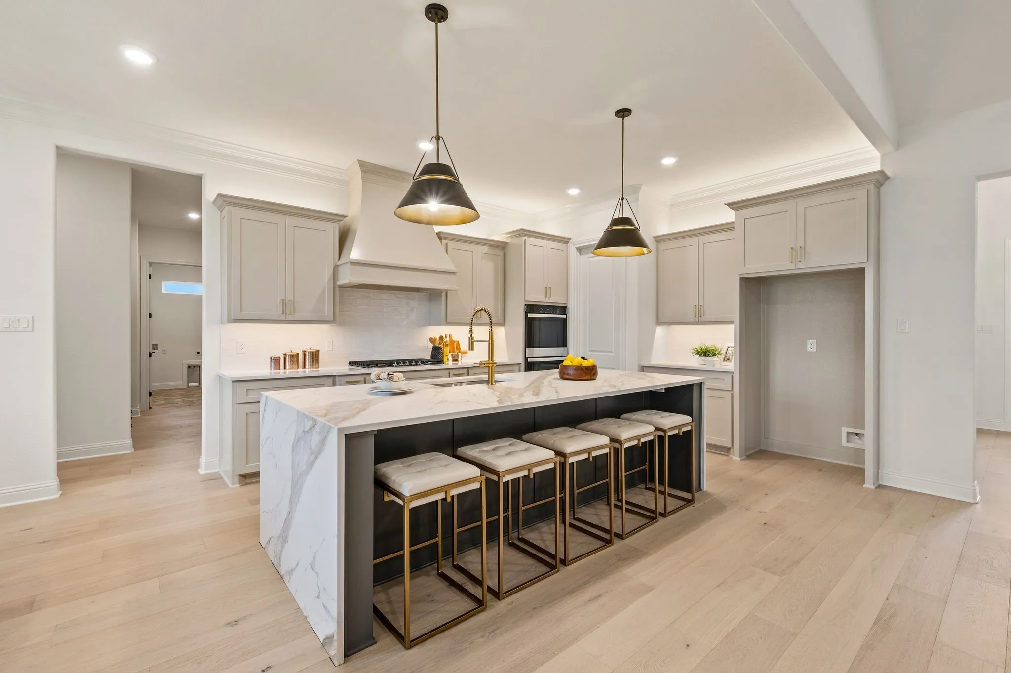 Spacious kitchen featuring a large waterfall island with seating, light wood-finish flooring, light gray cabinetry, recessed lighting, and modern pendant lighting