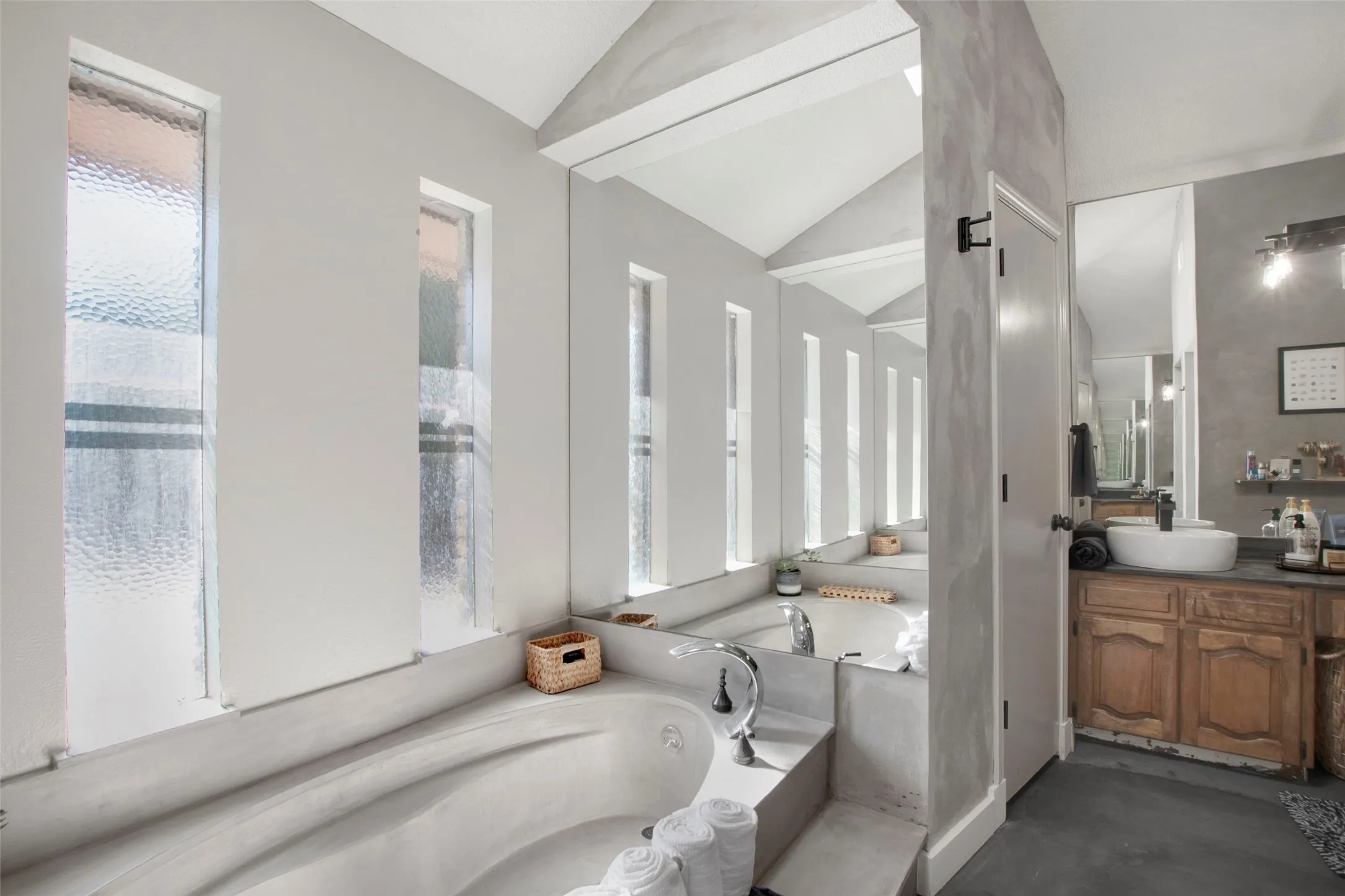 Bathroom featuring a bathing tub, concrete flooring, vanity, and vaulted ceiling