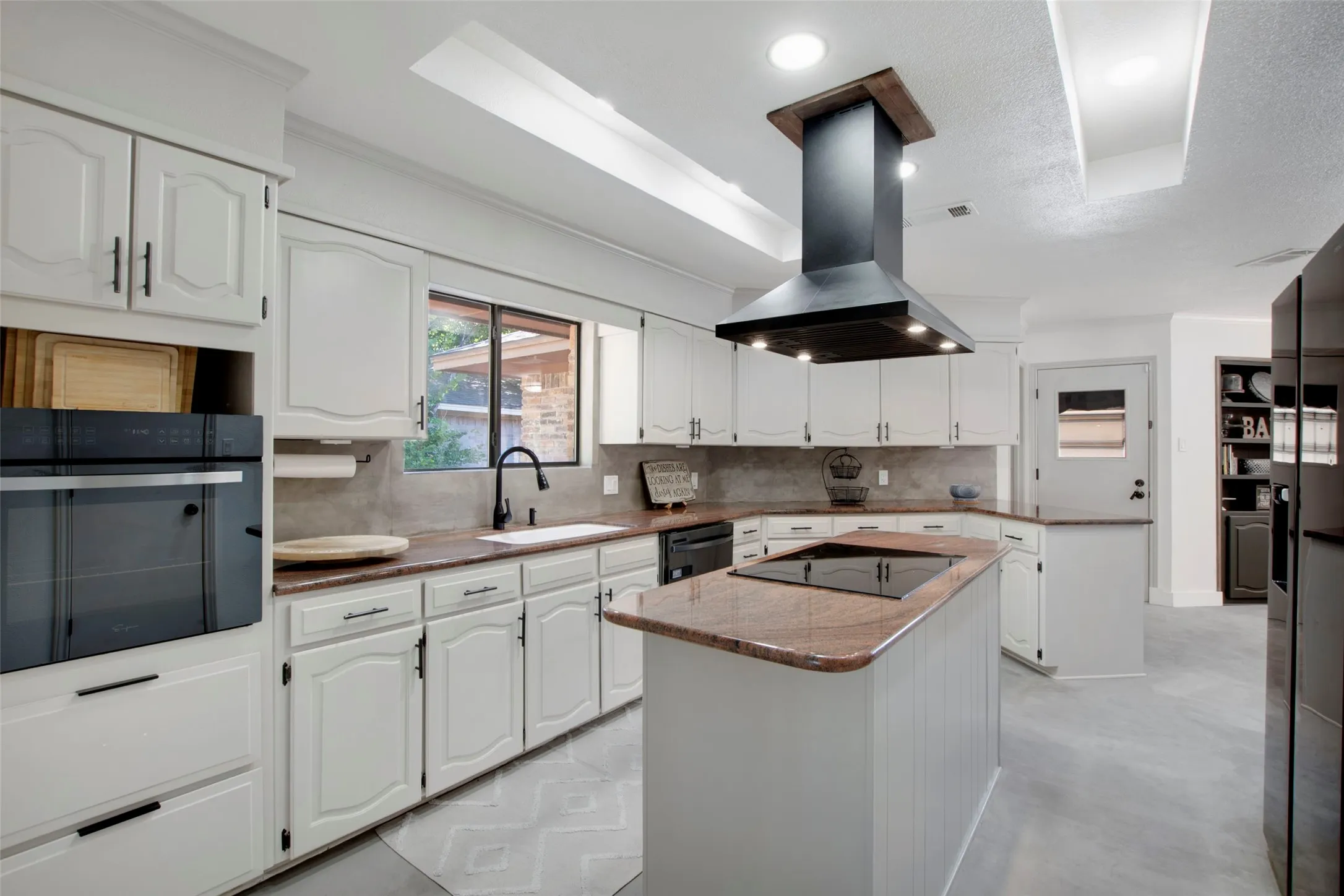 Kitchen featuring white cabinets, island exhaust hood, sink, and a kitchen island