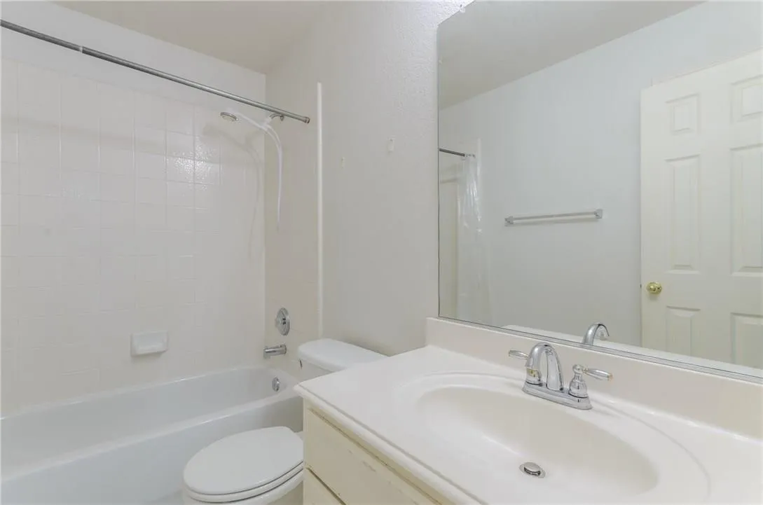Bathroom featuring a white bathtub with subway tile surround, chrome fixtures, a single-sink vanity with an integrated countertop, and a large mirror