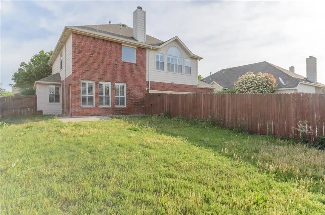 Expansive backyard featuring a privacy fence, concrete patio, and a two-story exterior with brick and siding finishes