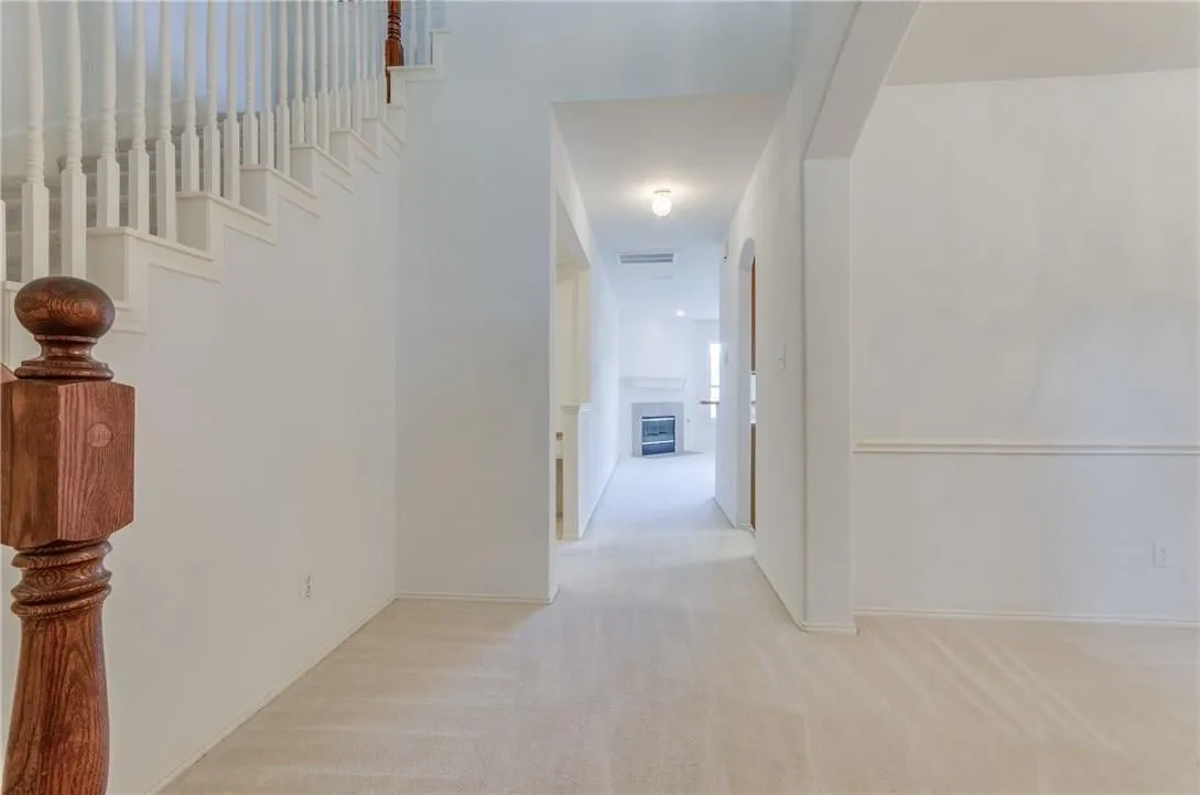 Entryway featuring a wood-finish newel post, white balusters, and a carpeted staircase