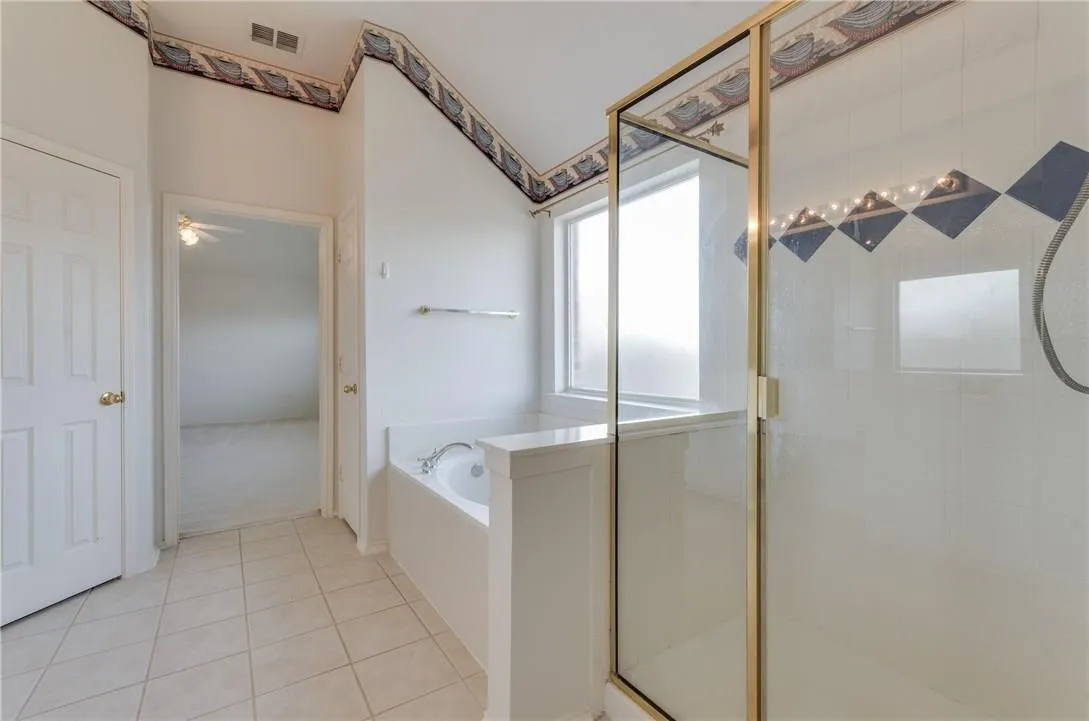 Bathroom featuring a built-in soaking tub, separate shower enclosure with a clear glass door, and a privacy window