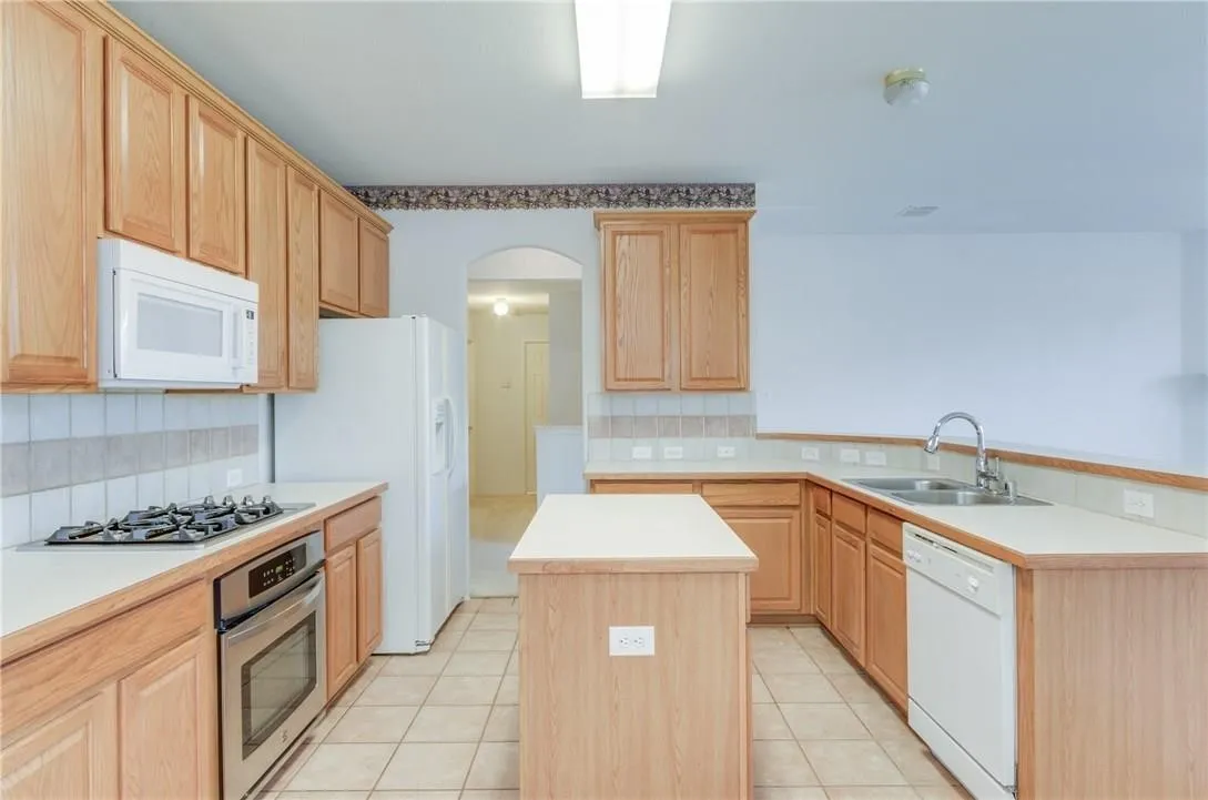 Kitchen featuring abundant wood cabinetry, light-toned countertops, a tile backsplash, and a built-in stainless steel oven with a gas cooktop