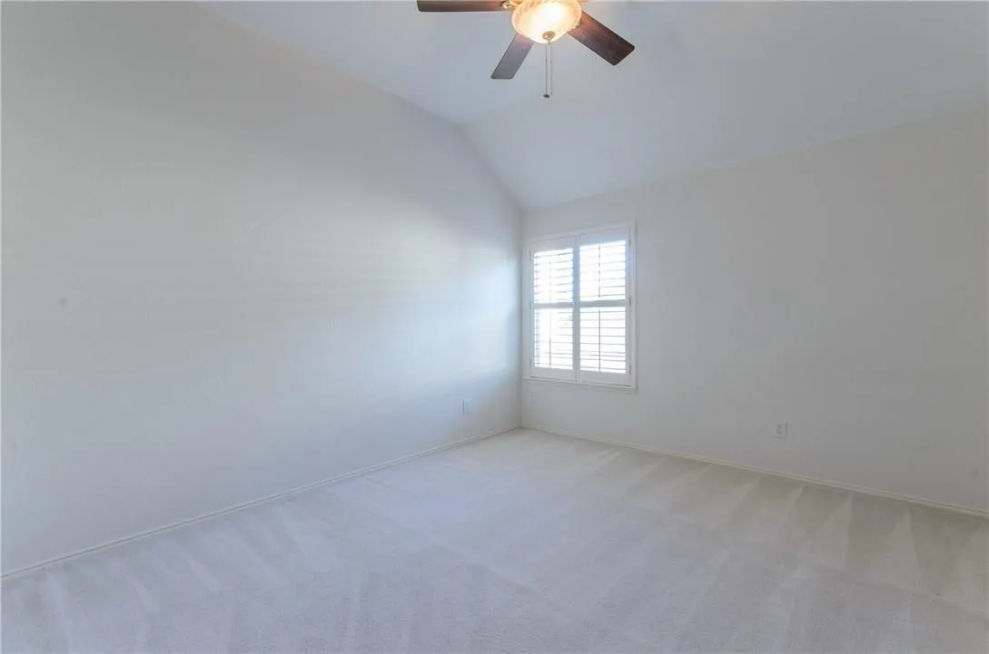 Carpeted room featuring a vaulted ceiling and a ceiling fan with integrated lighting