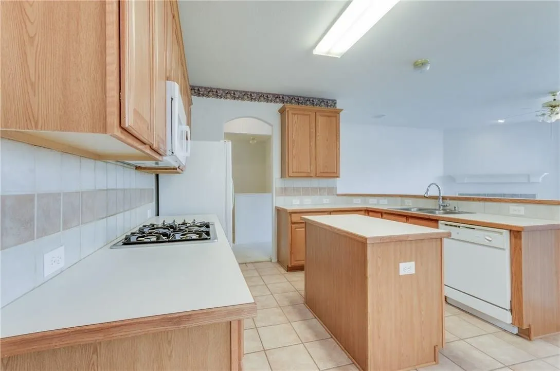 Kitchen featuring a gas cooktop, built-in microwave, tile flooring, wood cabinetry, and a central island