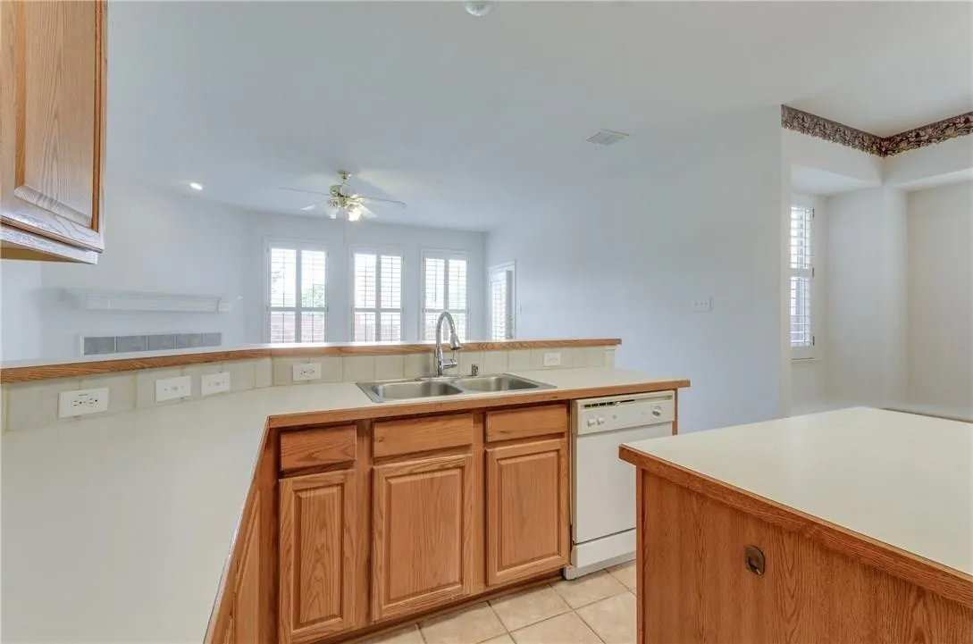 Kitchen featuring wood-finish cabinetry, a built-in dishwasher, and a double basin sink with a high-arc faucet