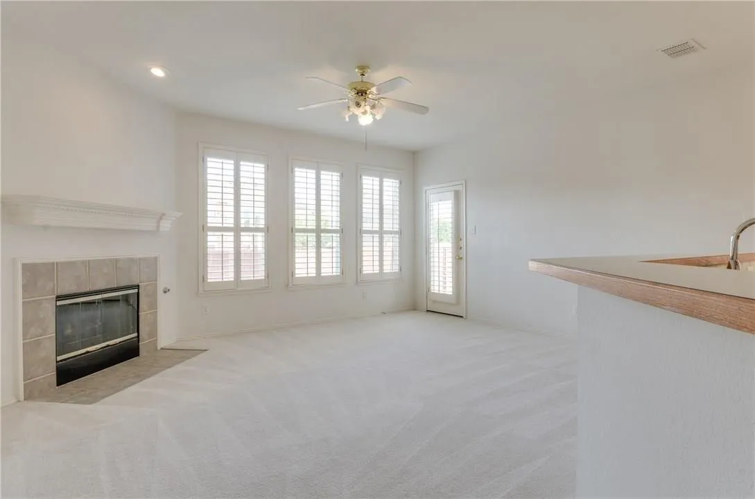 Living area featuring a tiled fireplace with mantel, three windows with plantation shutters, a ceiling fan with integrated lighting, recessed lighting, and a door providing exterior access