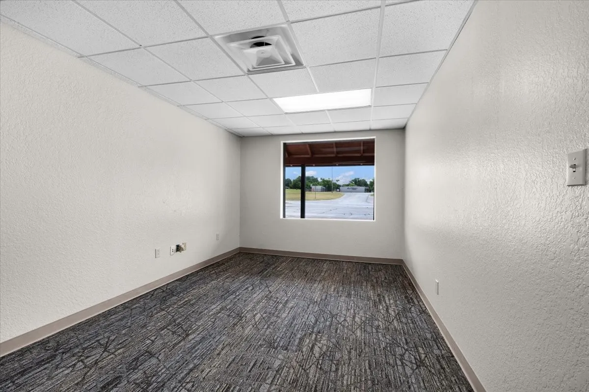 Office 1, featuring textured white walls, a drop ceiling with integrated lighting, and patterned carpet flooring