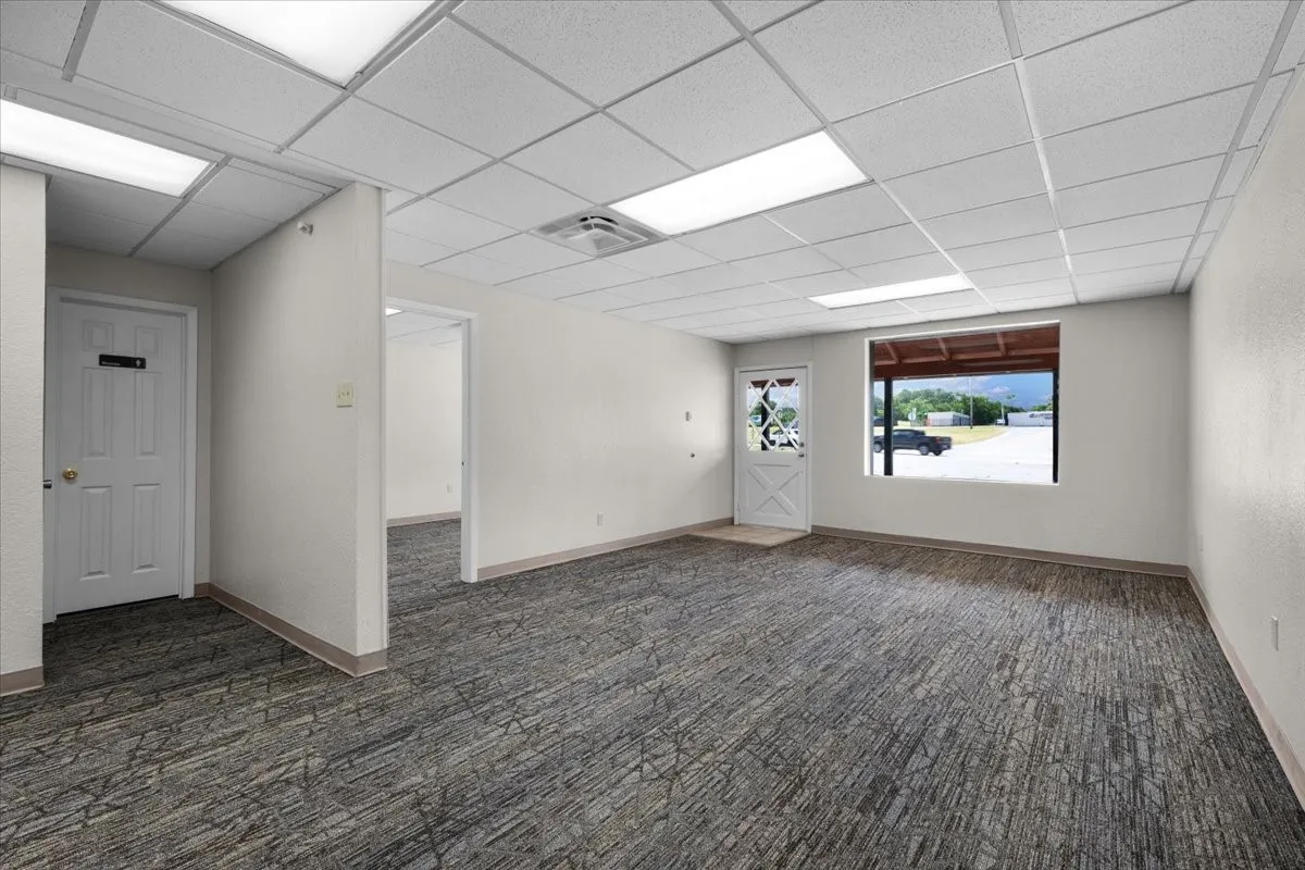 Spacious reception room featuring textured gray carpeting, white walls, and a drop ceiling with recessed lighting