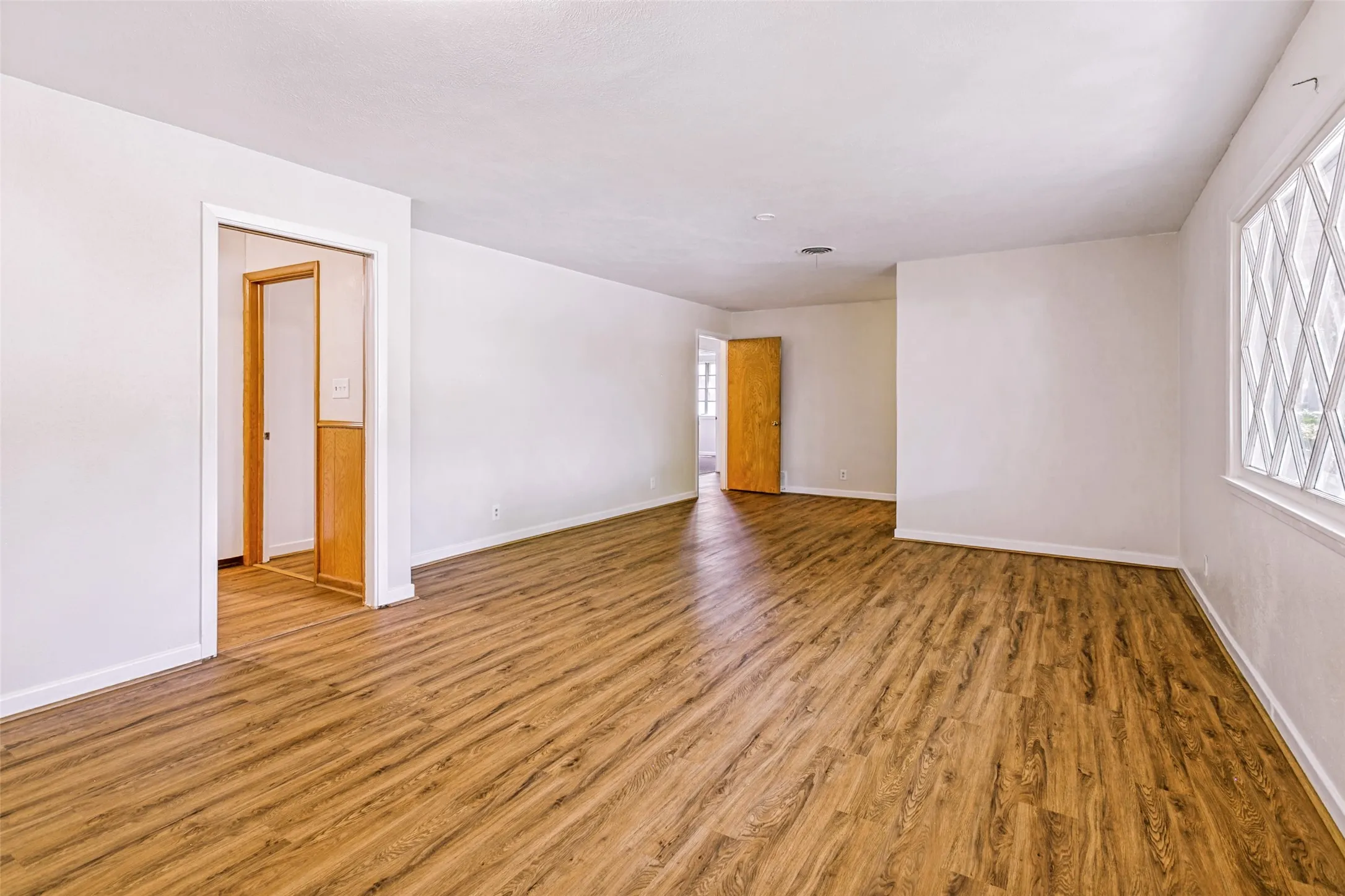 Spacious interior featuring wood-finish flooring, white walls, and a large window with diamond-patterned panes
