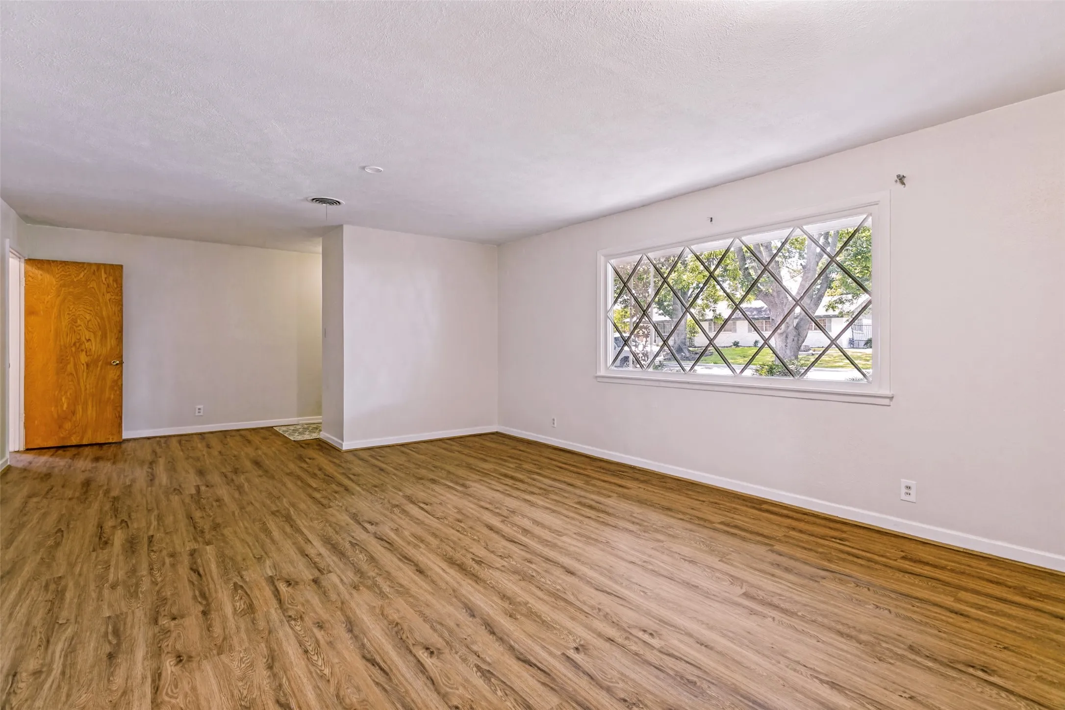 Spacious room featuring wood-finish flooring, white walls, and a large window with decorative mullions