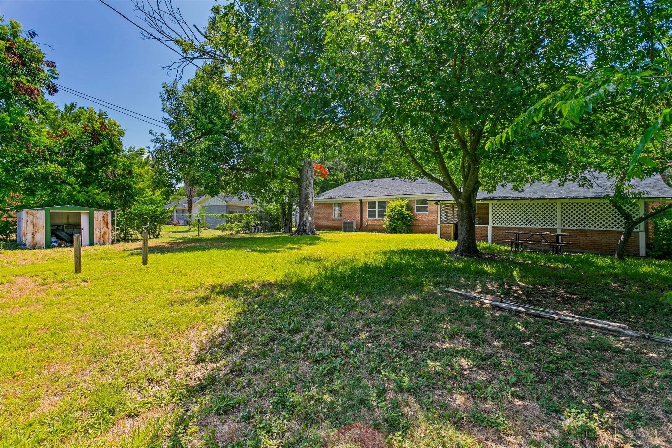Expansive backyard featuring mature trees, a manicured lawn, and a covered patio with lattice detailing