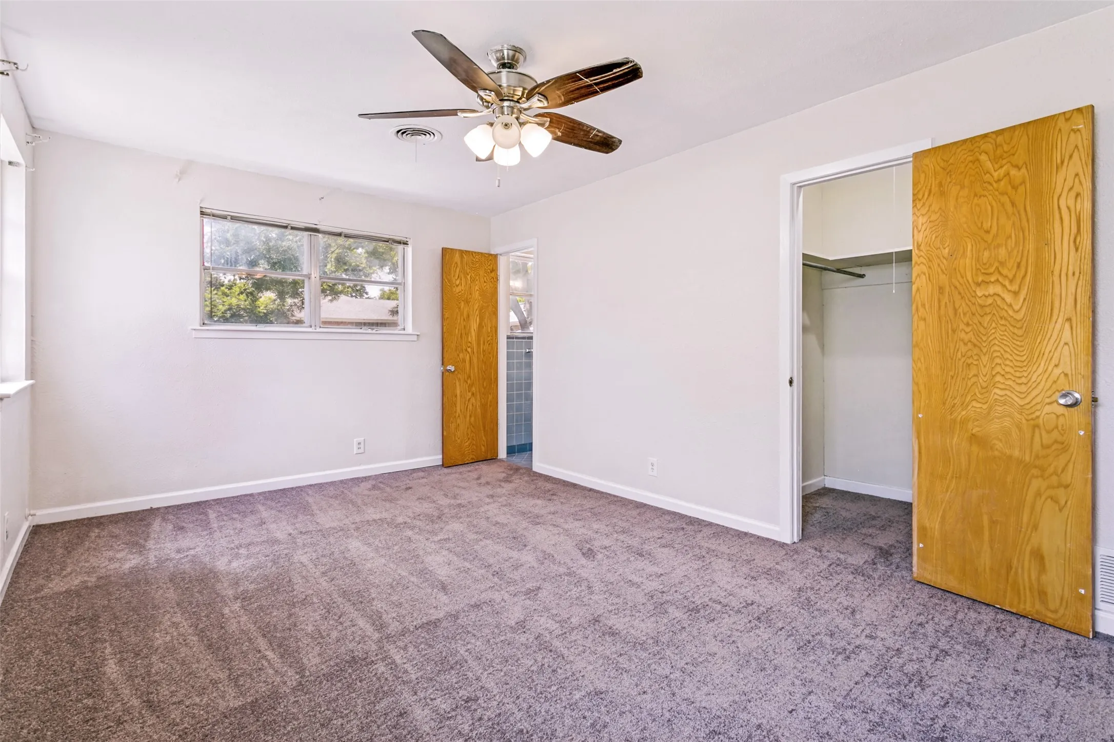 Carpeted room with a ceiling fan light fixture, two windows, and two wood-finish doors