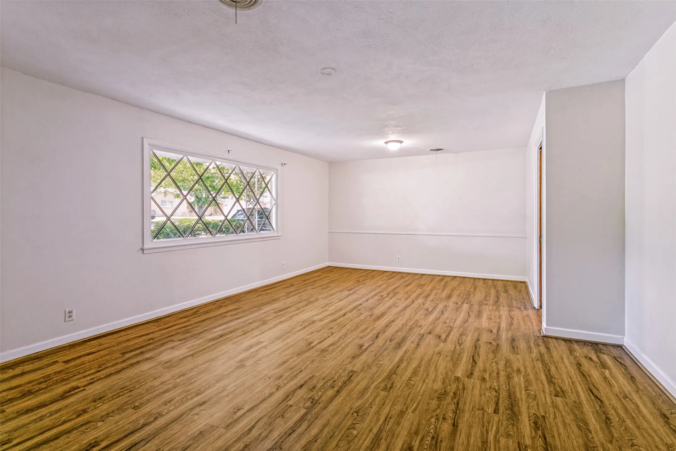 Spacious room featuring wood-finish flooring, a decorative lattice window, white baseboards, and a neutral color palette