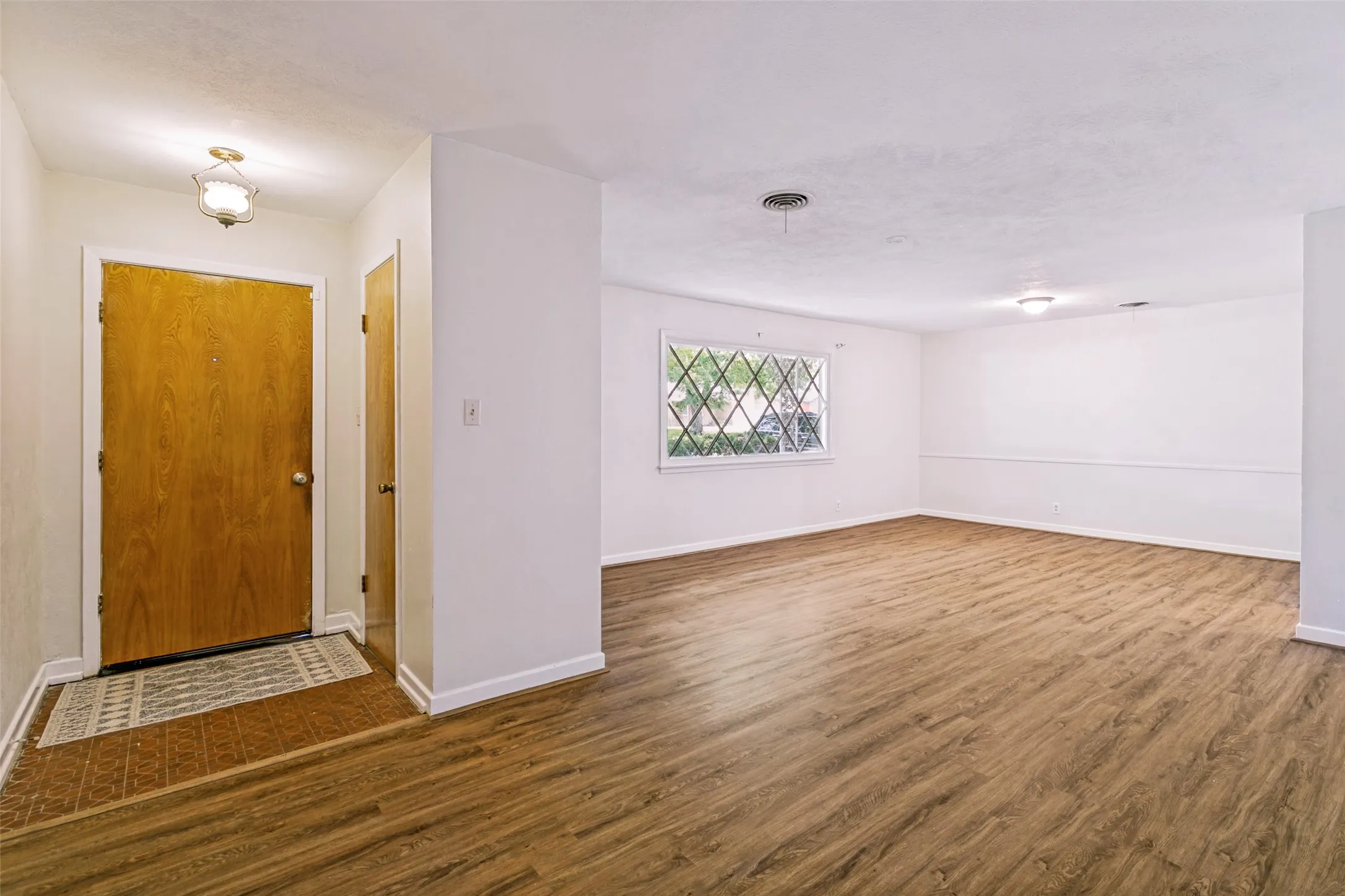 Spacious interior featuring wood-finish flooring, white walls, and a decorative window with a diamond-patterned grille