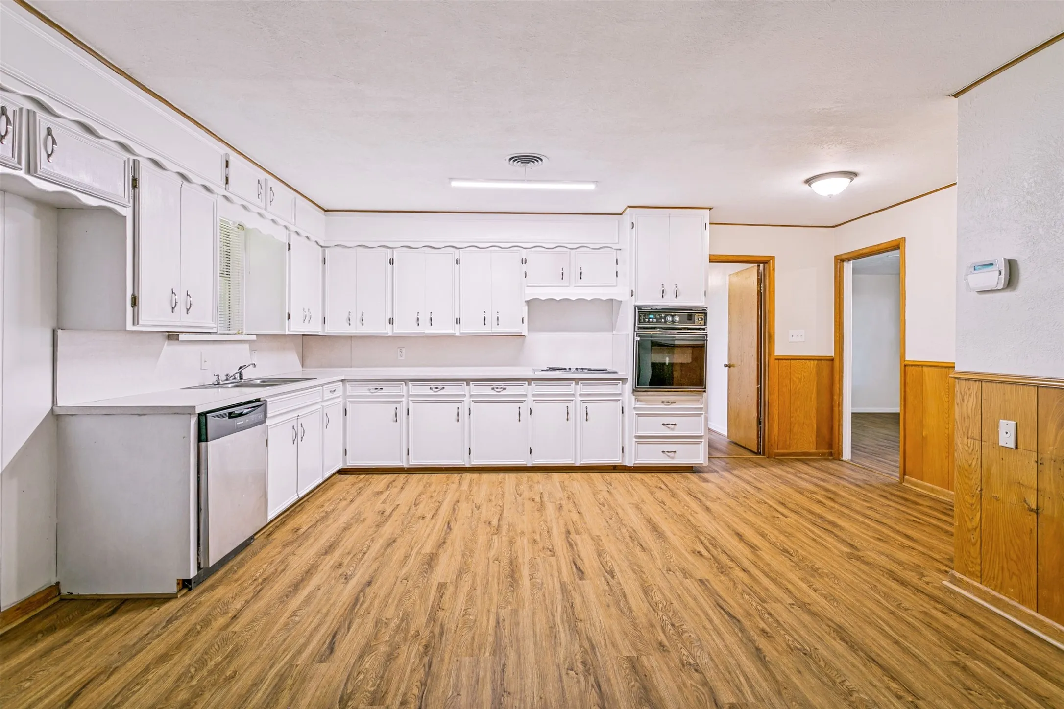 Spacious kitchen featuring extensive white cabinetry, wood-finish flooring, a built-in oven, and a stainless steel dishwasher