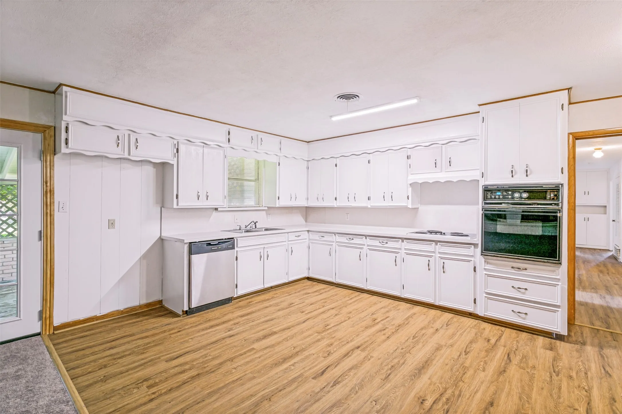 Kitchen featuring extensive white cabinetry, wood-finish flooring, a built-in wall oven, and a stainless steel dishwasher