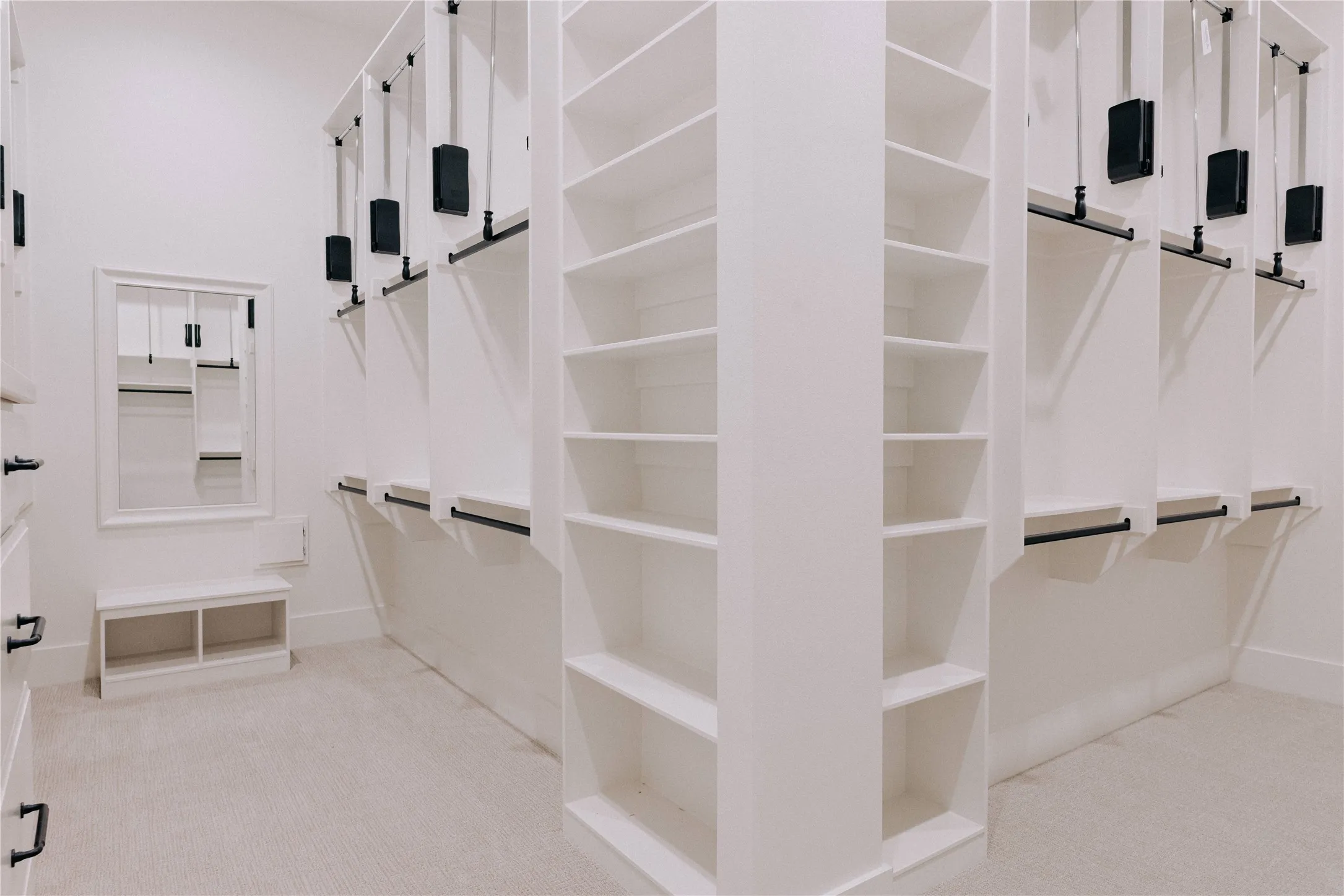 Spacious walk-in closet featuring extensive built-in shelving, multiple hanging rods, pull-down clothing lifts, a framed mirror, and a built-in bench seat