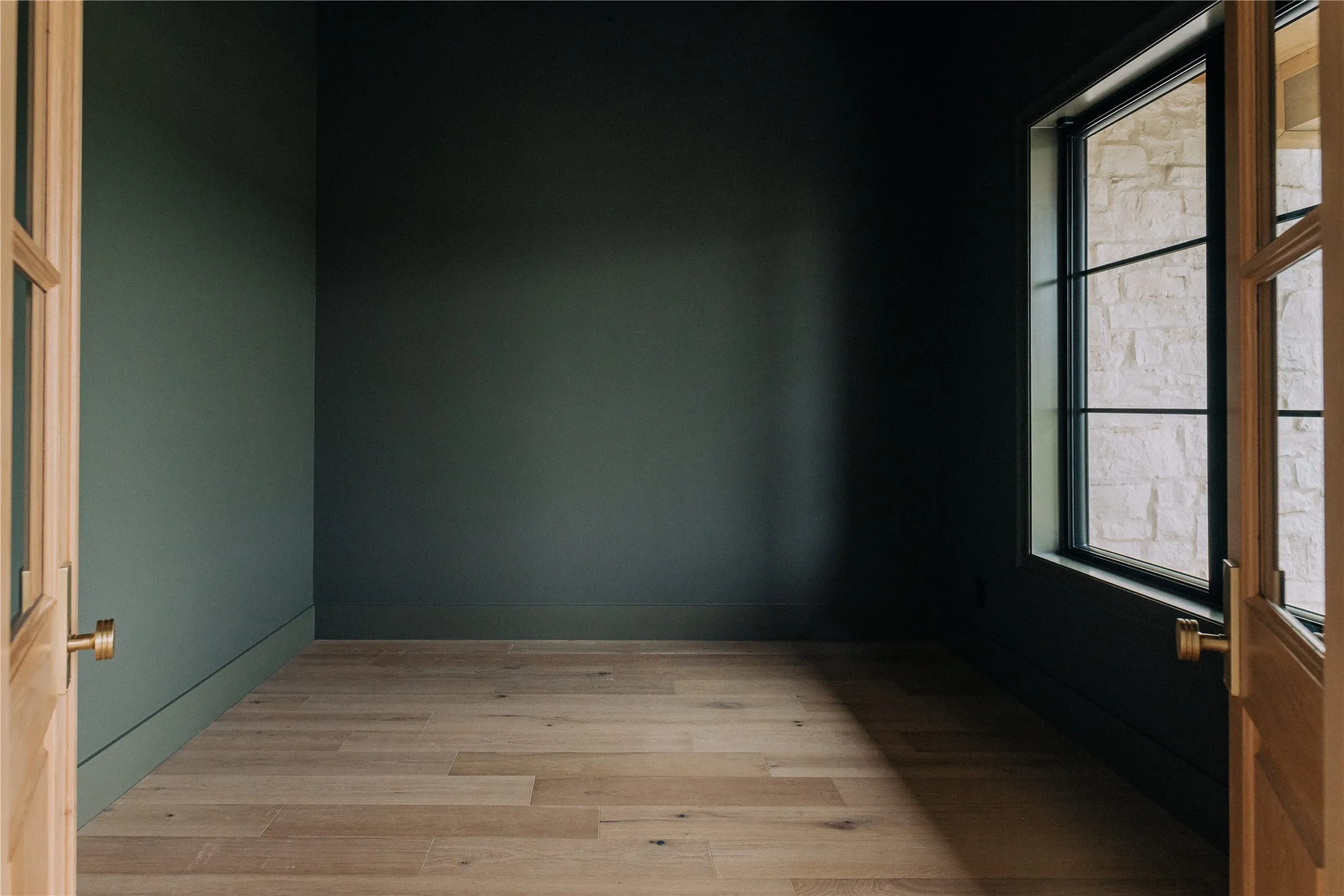 Room featuring rich green walls, light wood-finish flooring, and a large window with dark grilles