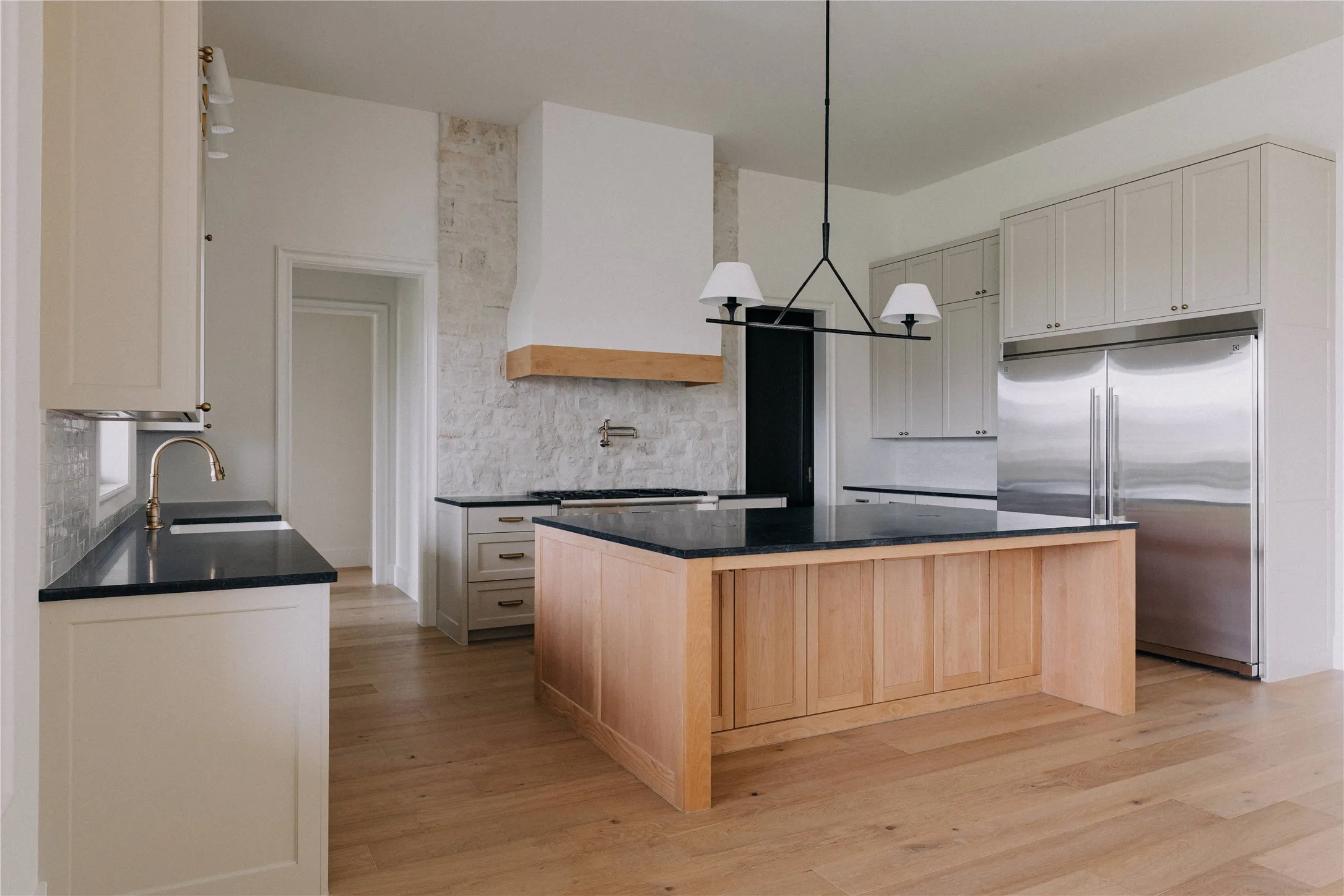 Contemporary kitchen featuring a substantial wood-finish island with black countertop, stainless steel appliances including a side-by-side refrigerator, and a white subway tile backsplash