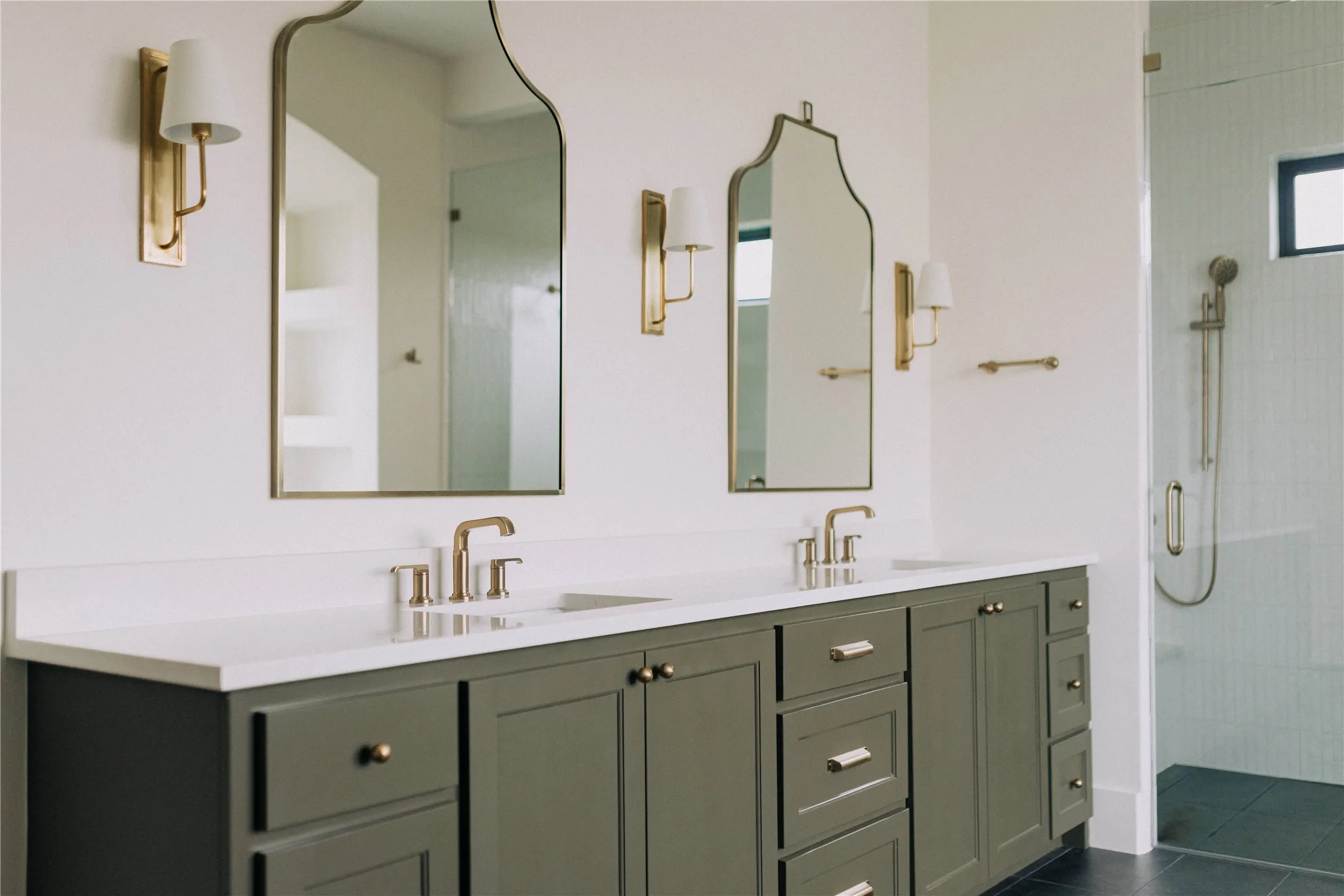 Spa-inspired primary bathroom showcasing a custom dual-vanity with sage-green cabinetry, white quartz countertops, and brushed brass hardware and fixtures