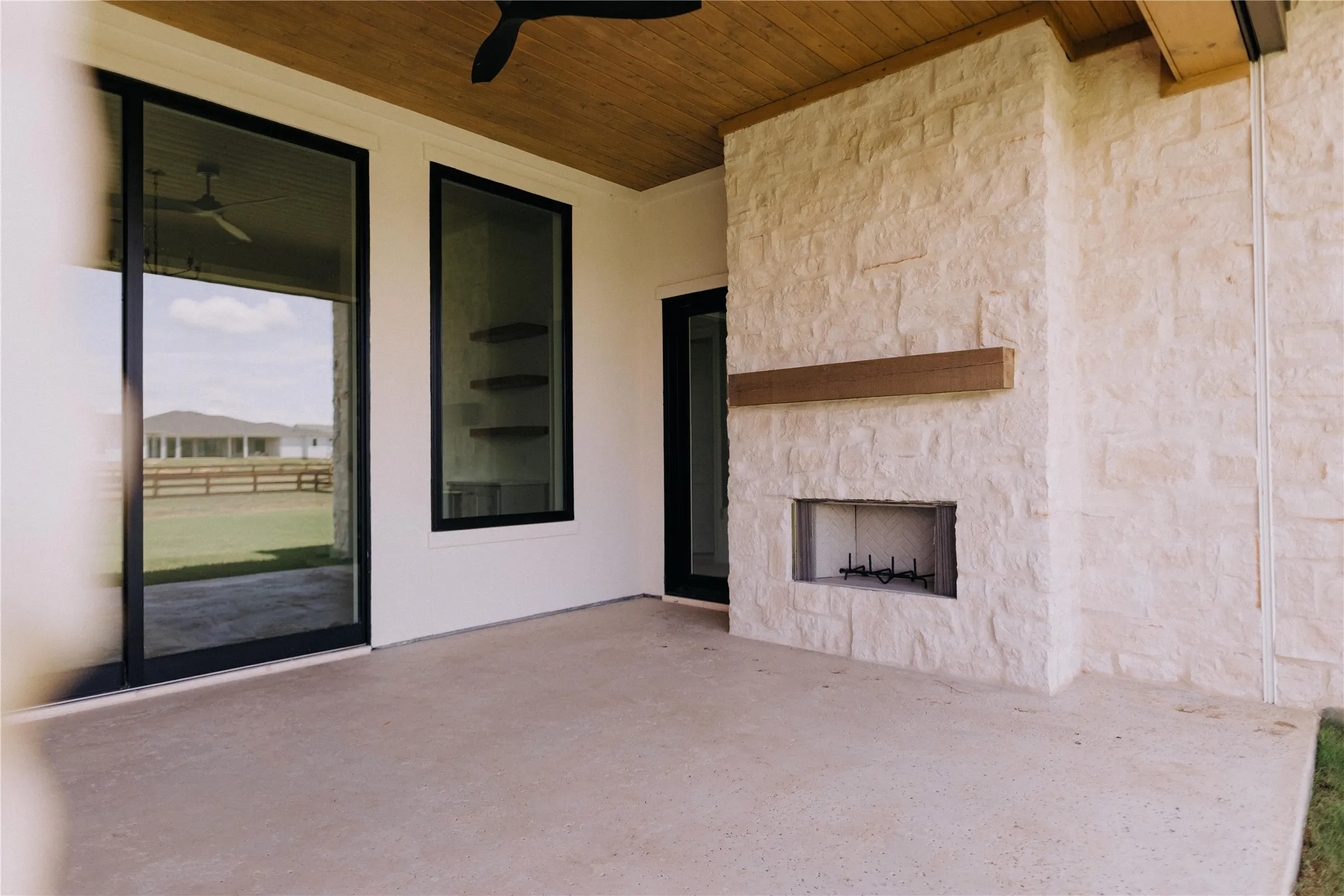Outdoor patio featuring an integrated stone fireplace with a wood mantle, a wood-paneled ceiling, and concrete flooring