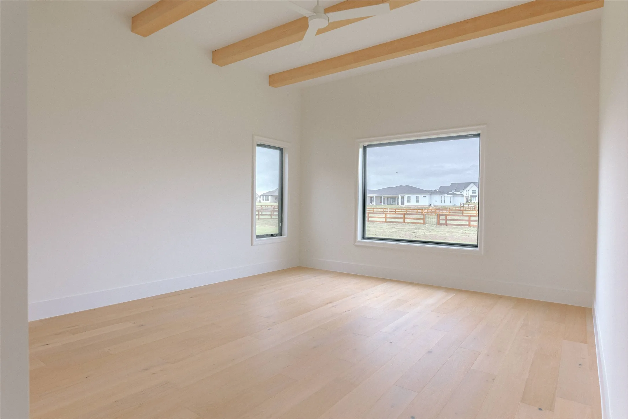 Spacious room featuring vaulted ceilings with exposed wood beams, light wood-finish flooring, and white baseboards