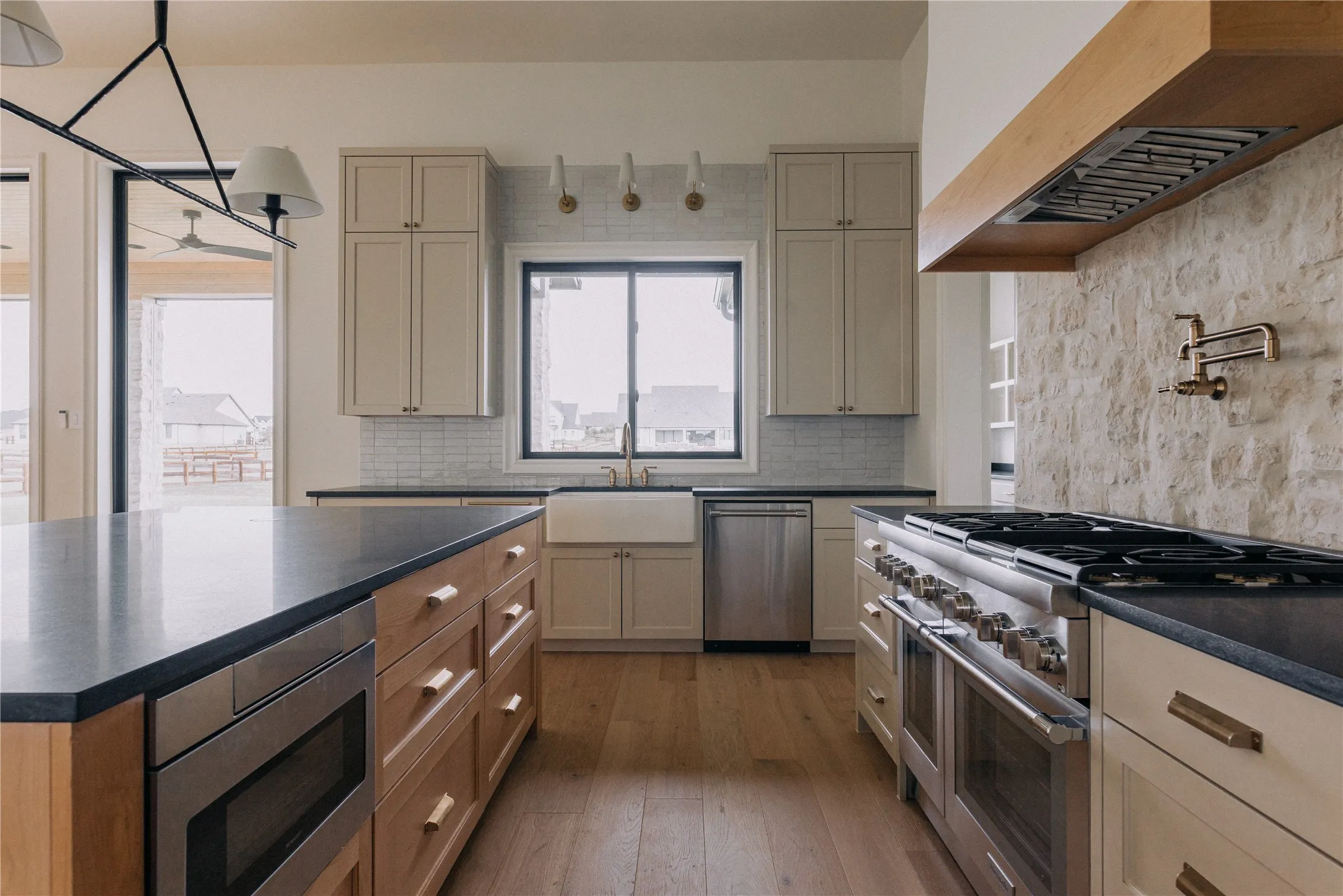 Gourmet kitchen featuring a large island with built-in microwave, stone accent wall with pot filler, stainless steel professional-grade range, farm sink, and wood-finish flooring
