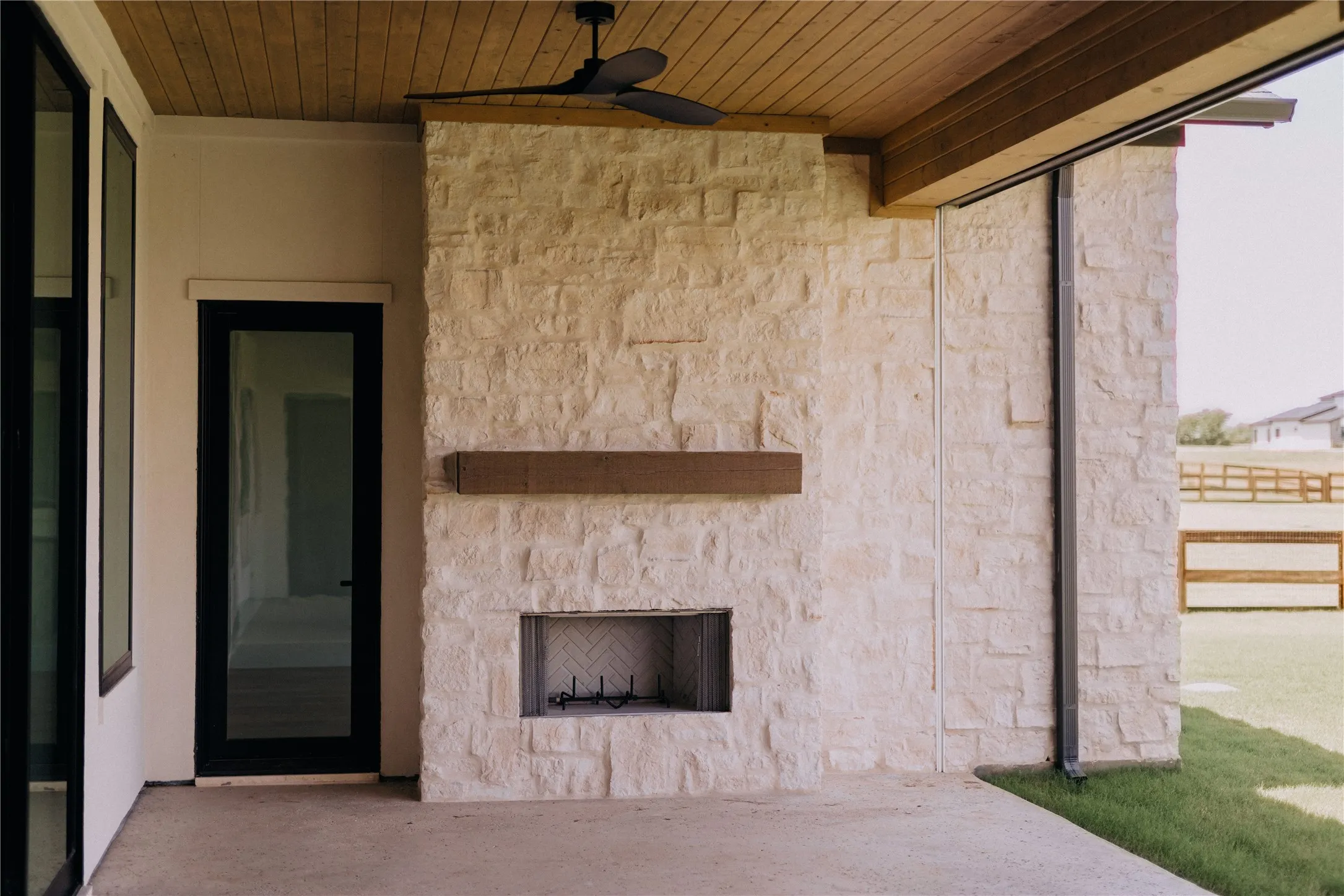 Outdoor patio featuring a stone fireplace with a wood mantle, concrete flooring, wood-paneled ceiling, and a ceiling fan