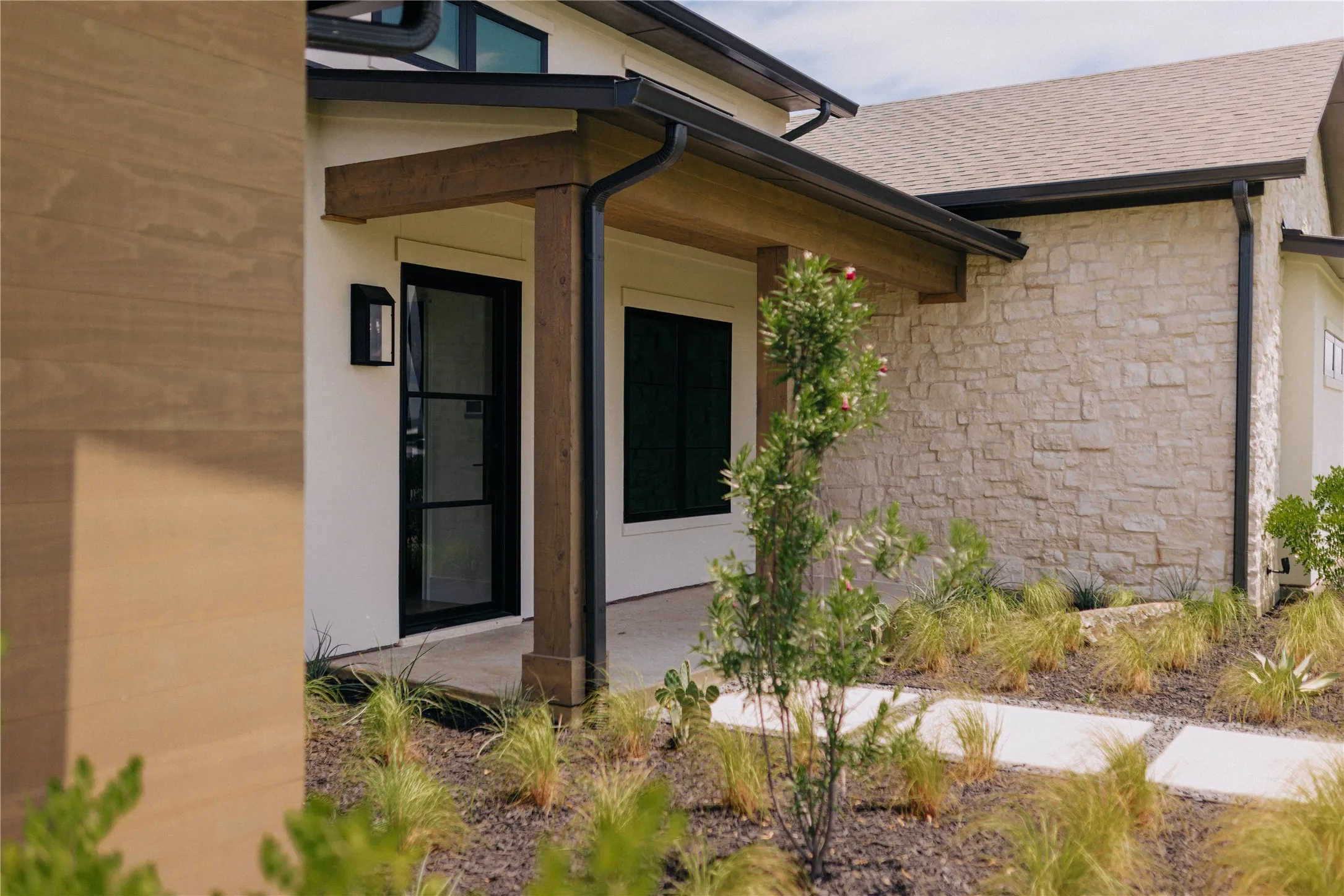 Modern front entry featuring a clean architectural design with a covered portico, black-framed glass door, and contemporary brick and stucco exterior