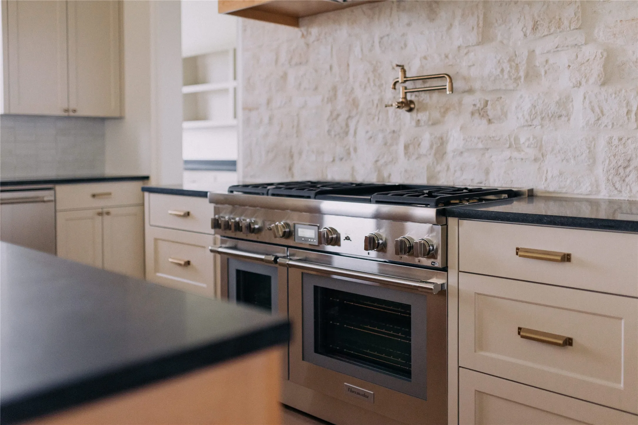 Gourmet kitchen featuring a stainless steel range with double ovens, a stone-finish backsplash, and a wall-mounted pot filler