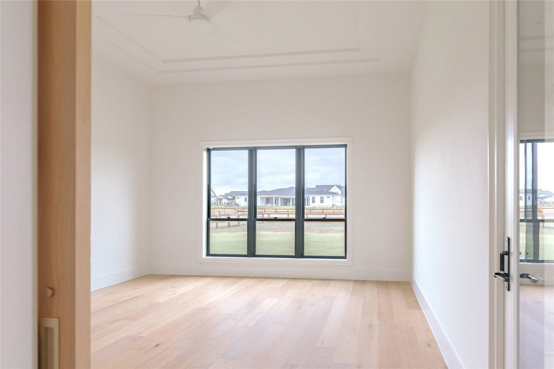 Bright room featuring wood-finish flooring, a large window with dark trim, a ceiling fan, and a tray ceiling with crown molding