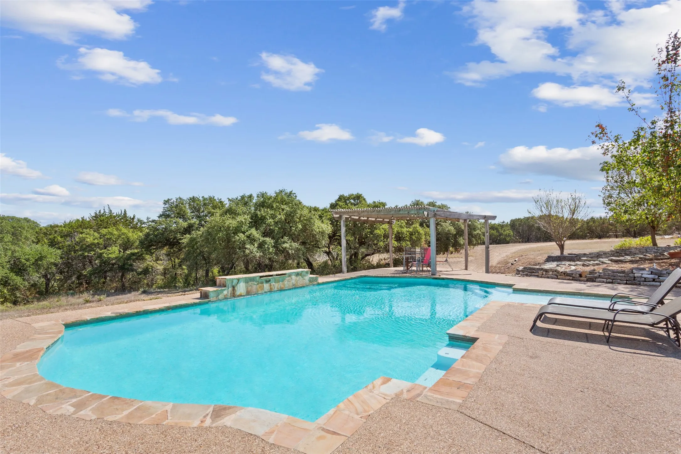 Expansive outdoor pool area featuring a freeform swimming pool with a stone coping, a built-in waterfall feature, and a pergolated patio space