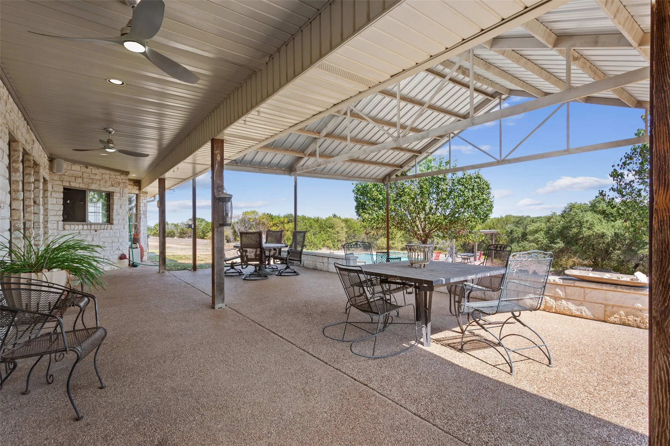 Expansive covered patio featuring a metal roof structure, ceiling fans, and an exposed aggregate concrete surface
