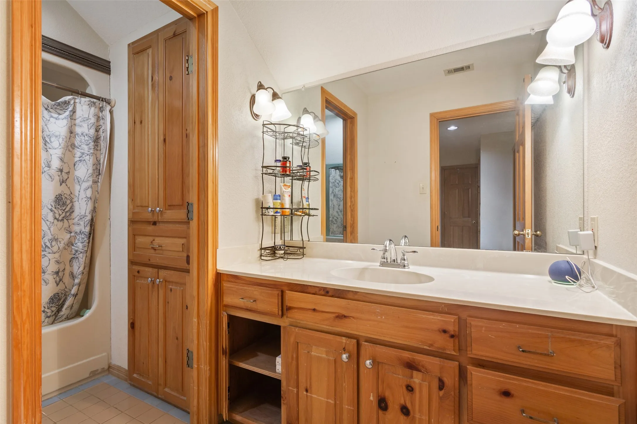 Bathroom featuring a single vanity with an integrated sink, light-toned countertop, and natural wood cabinetry