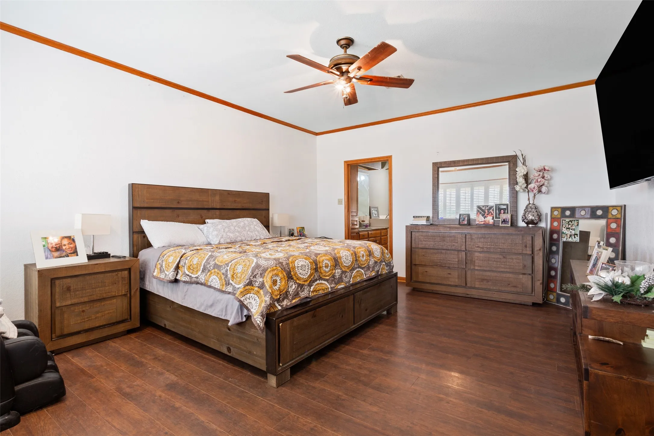 Spacious bedroom featuring wood-finish flooring and white walls with a contrasting wood trim accent
