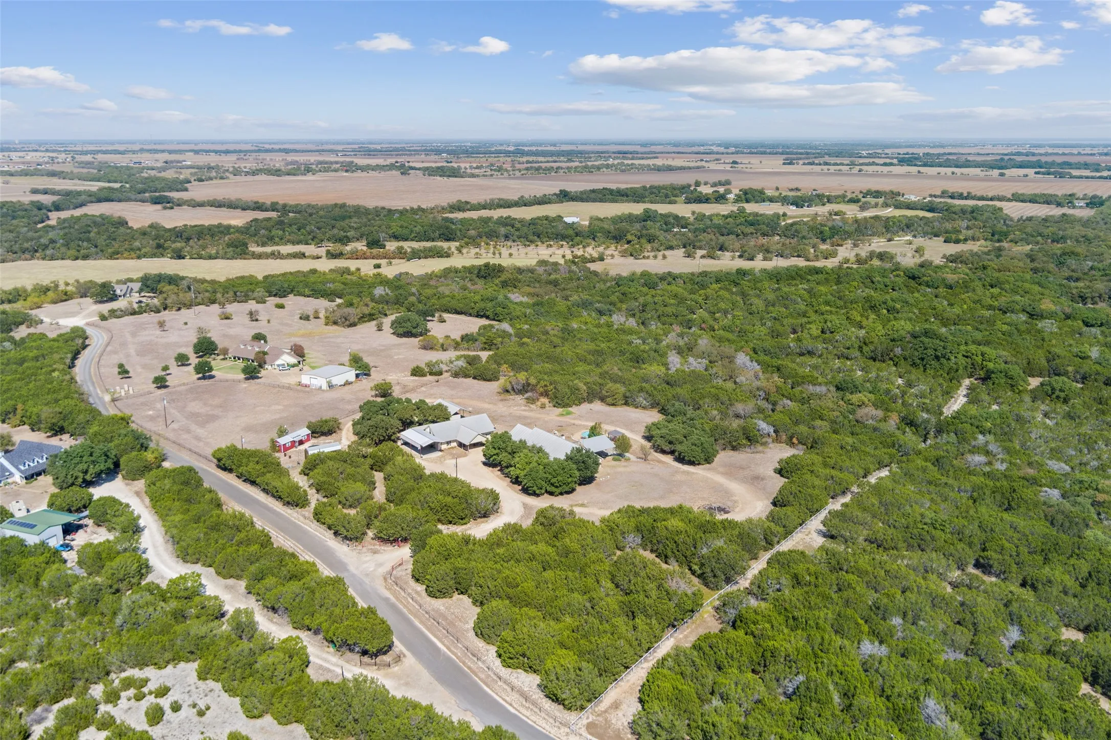Expansive property featuring natural tree coverage, paved road frontage, multiple structures, and cleared open land