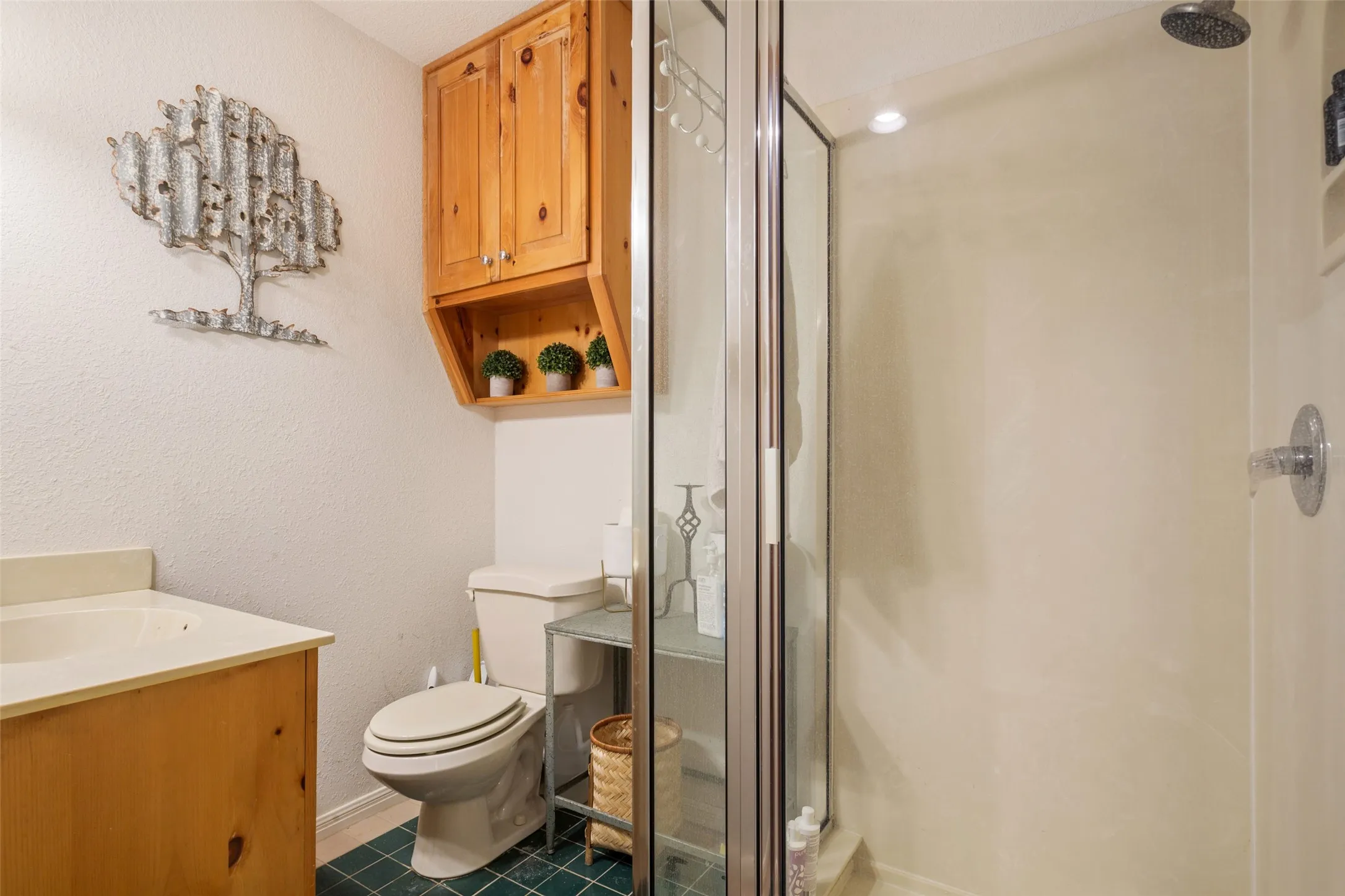 Bathroom featuring a glass-enclosed shower, a wood-finish vanity with an integrated sink, and an overhead wood-finish cabinet with open shelving