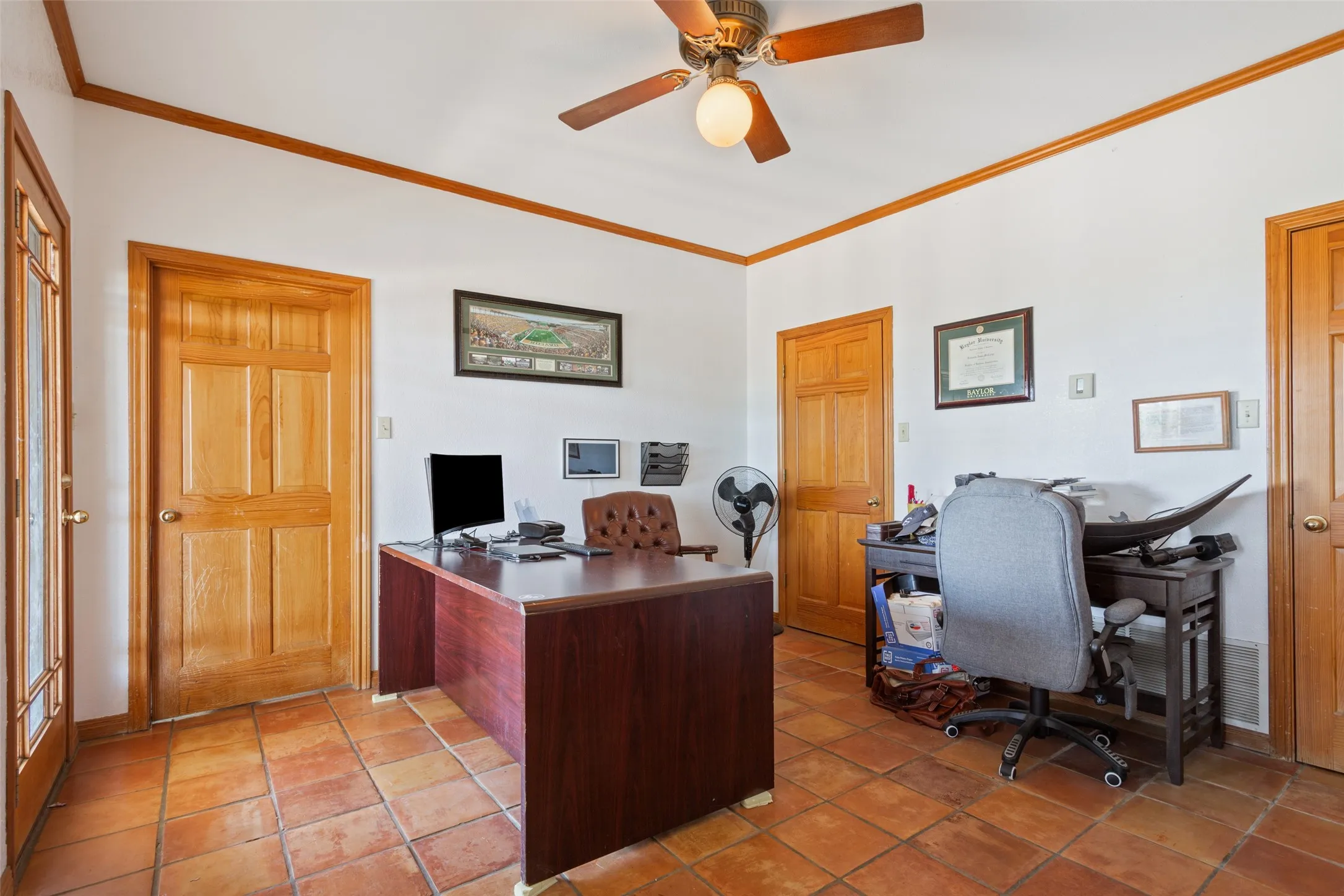Bright room featuring terra cotta tile flooring, light wood trim, and a ceiling fan with integrated lighting