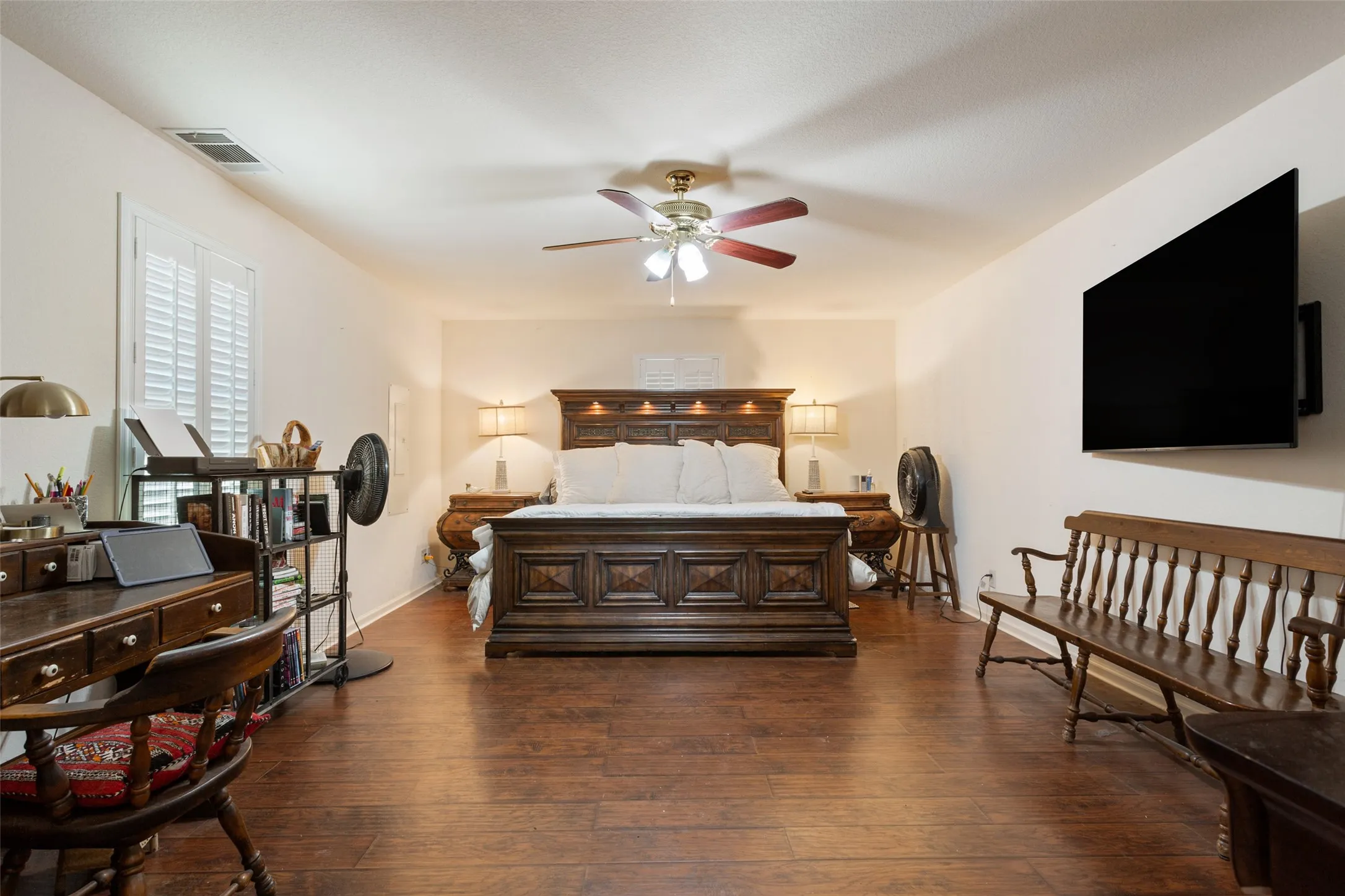 Spacious room featuring wood-finish flooring, a ceiling fan, and white plantation shutters on the window