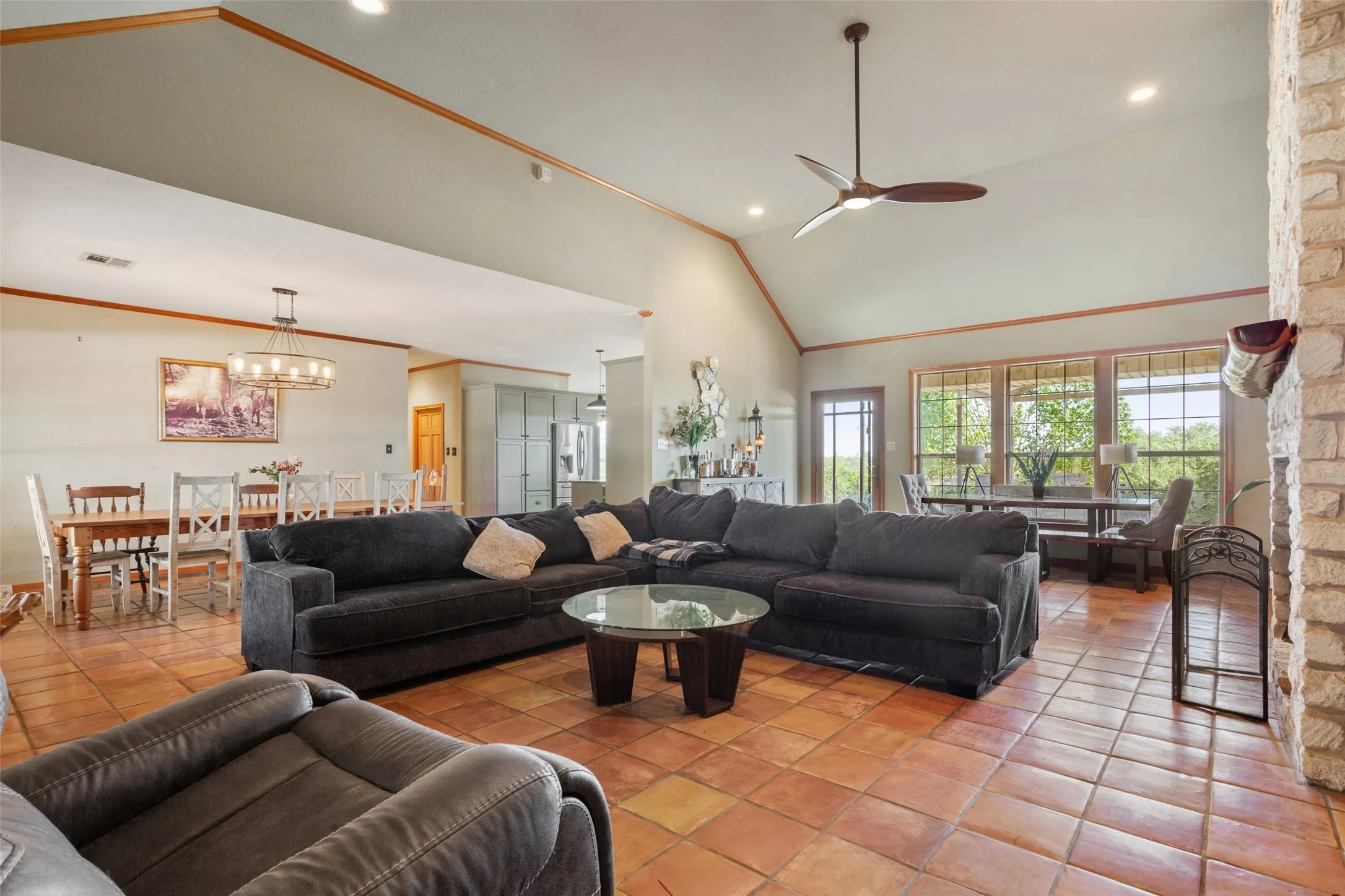 Spacious living area featuring terra cotta flooring, a vaulted ceiling with a modern ceiling fan, and a stone-clad fireplace