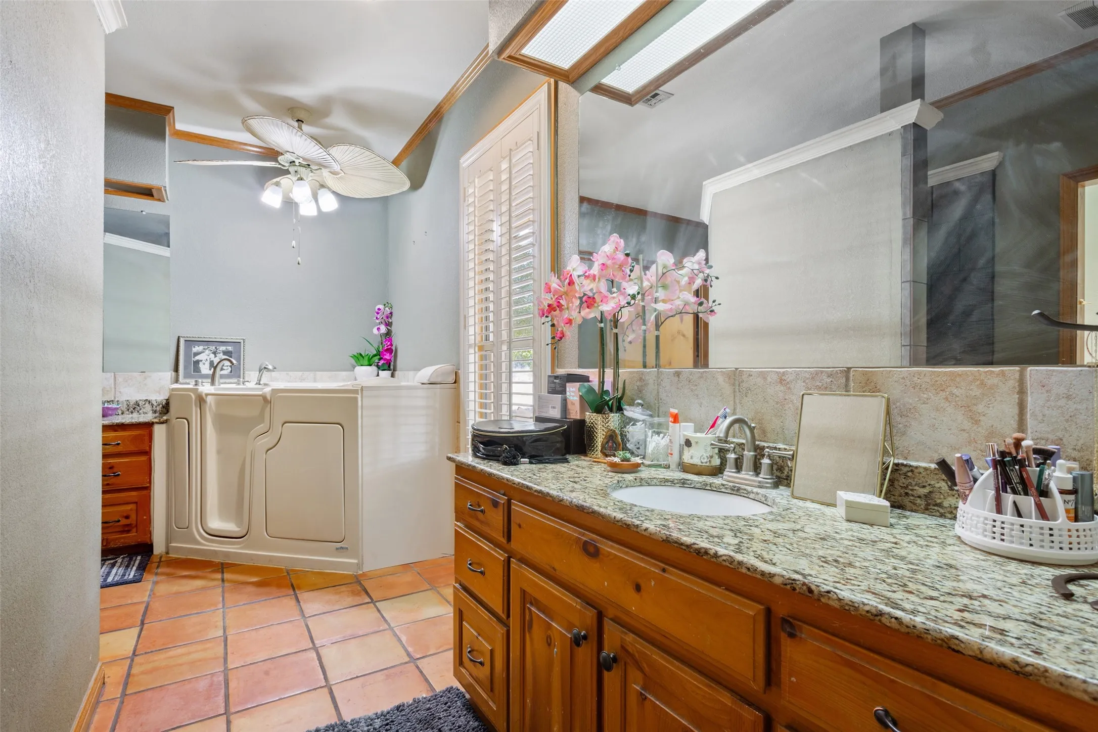 Bathroom featuring a walk-in tub, terracotta tile flooring, wood cabinetry, granite countertops, and a ceiling fan