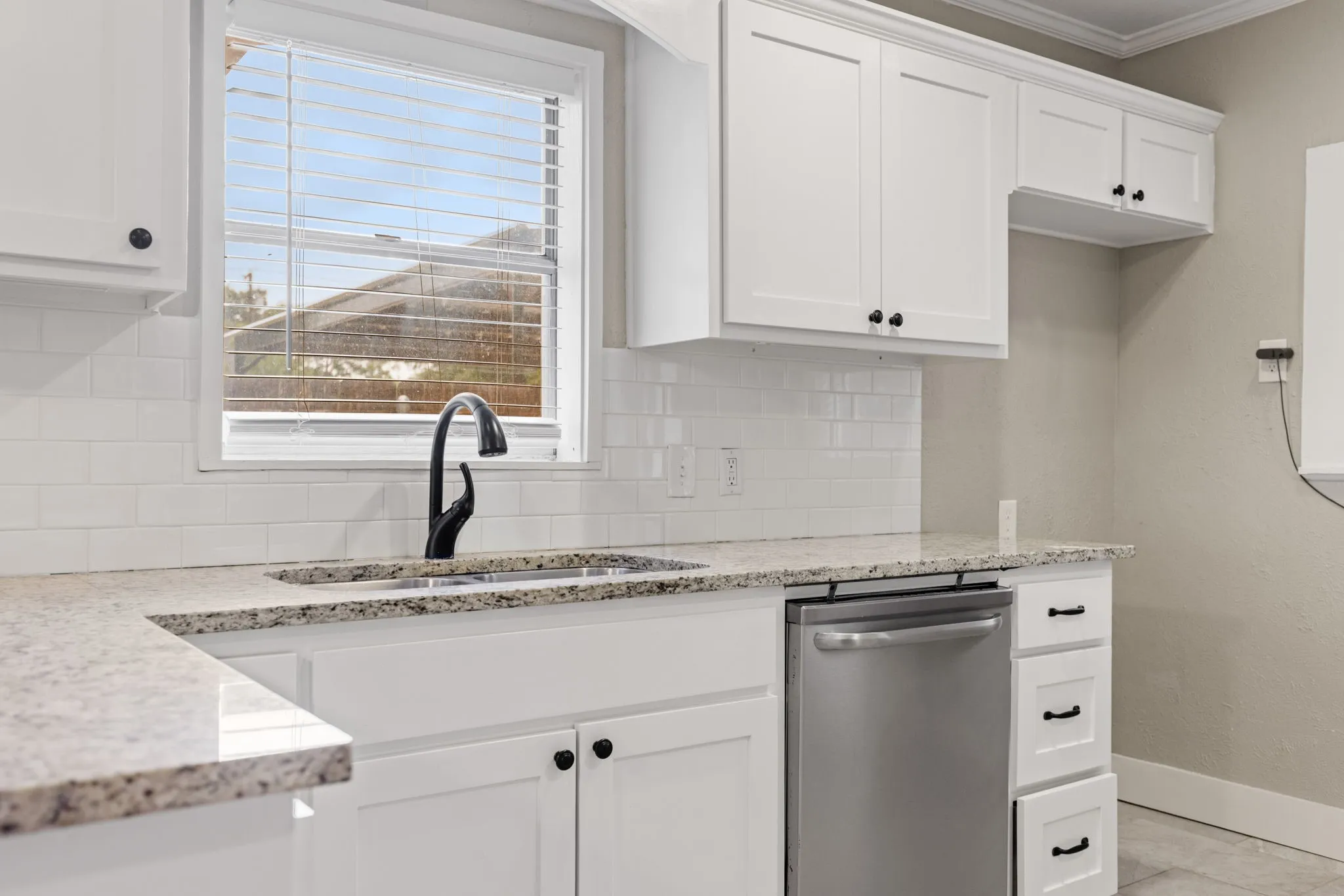 Kitchen featuring white shaker-style cabinetry, granite-style countertops, a stainless steel dishwasher, a single basin sink with a matte black gooseneck faucet, and a white subway tile backsplash