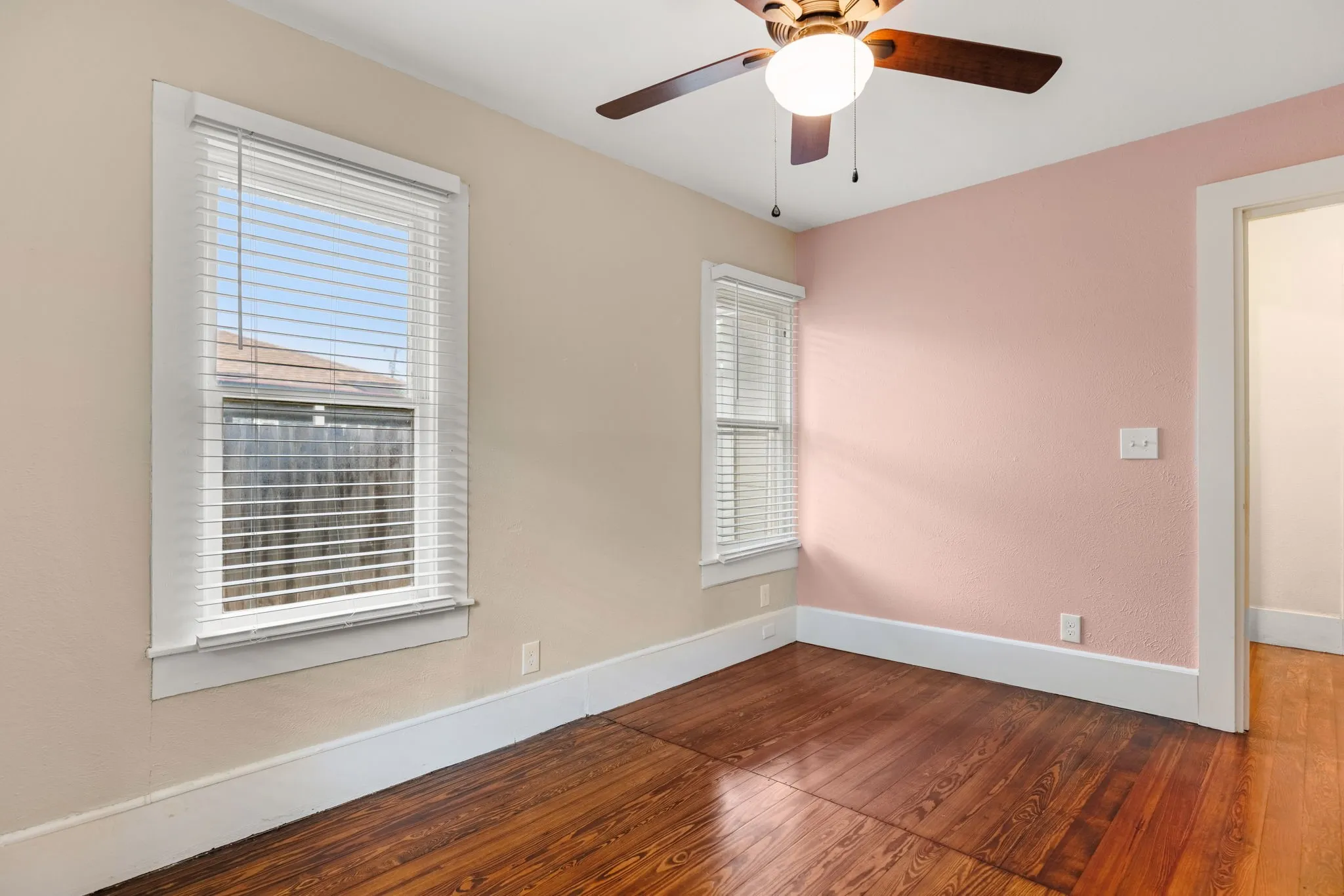 Room featuring wood-finish flooring, two windows with blinds, a ceiling fan with light fixture, and contrasting wall colors